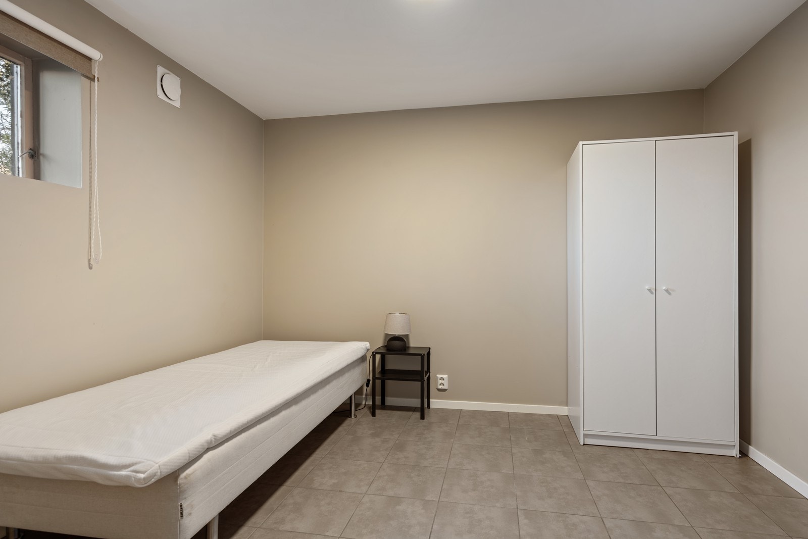 Soverom/bod med flislagt gulv og varmekabler. Vinduet her er sprukket. Rullegardin i vindu. Dobbelt garderobeskap. Galleribilde