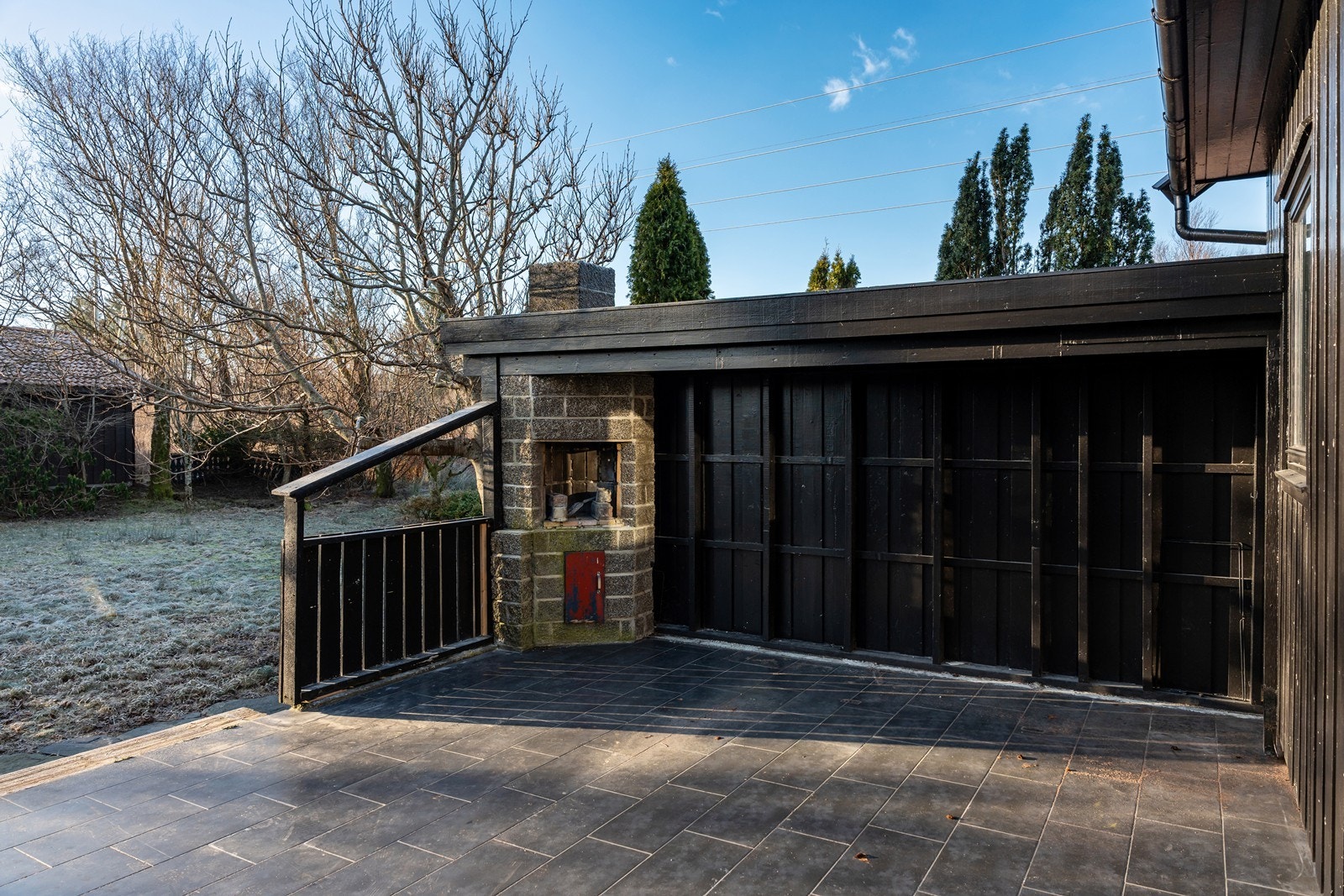 Skyvedør fra stua og ut til romslig flislagt terrasseområde med peis og levegg. Galleribilde