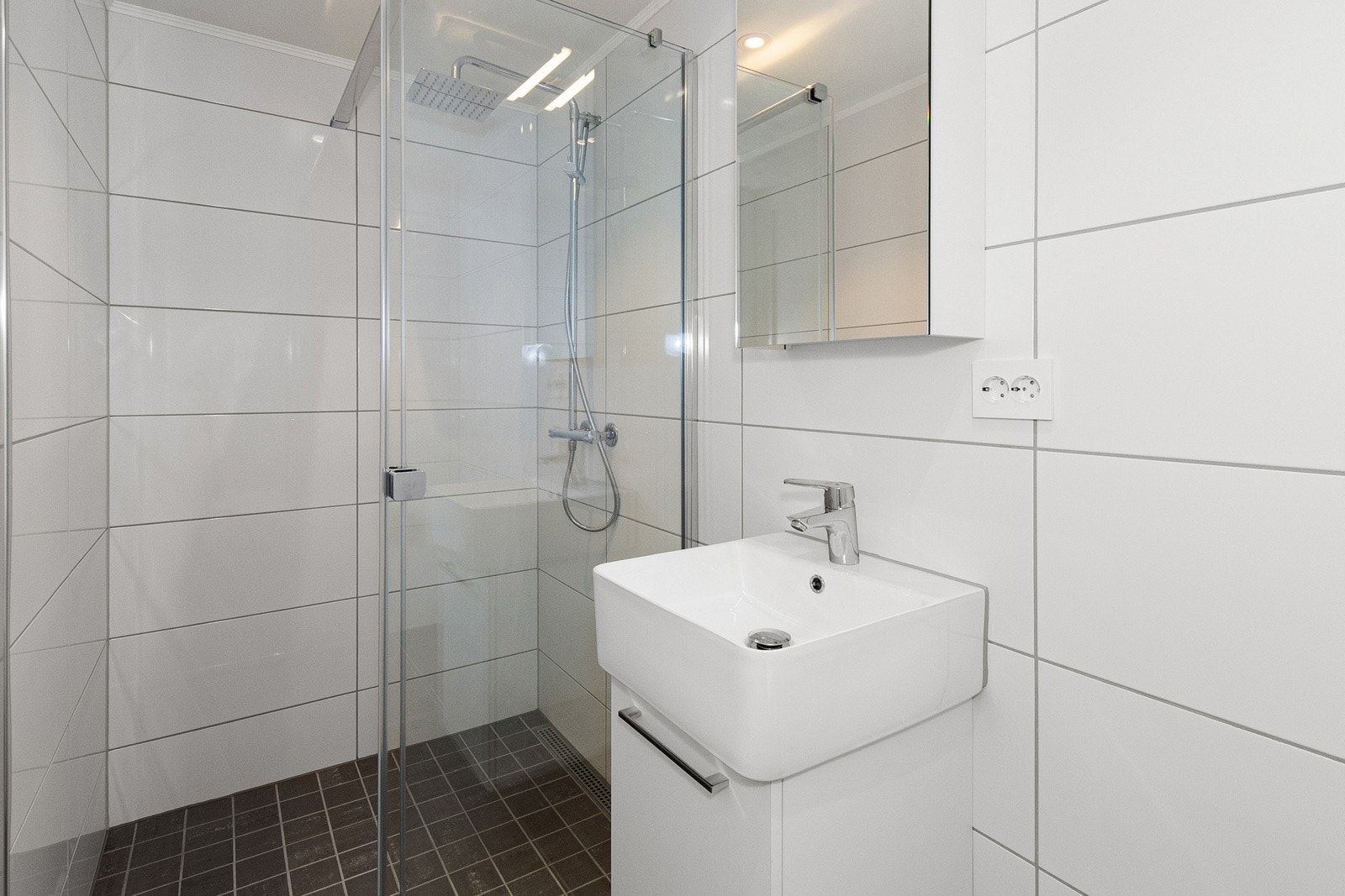 Bad nr 2 med dushjørne med foldedører, servant, speil og vegghengt toalett. Galleribilde