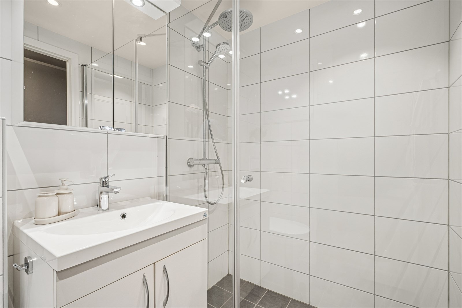 Baderomsinnredningen inneholder nedfelt servant, vegghengt speilskap, vegghengt toalett og dusjhjørne med glassvegger, samt opplegg for vaskemaskin. Galleribilde