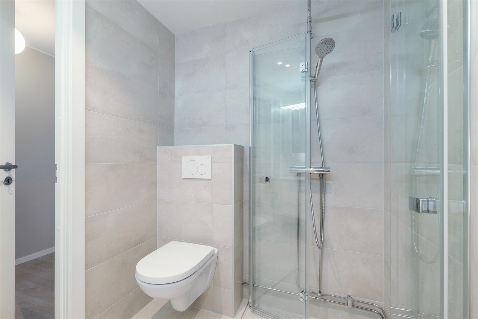 Badet er utstyrt med vegghengt toalett og en romslig dusjløsning med innfellbare glassdører. Galleribilde