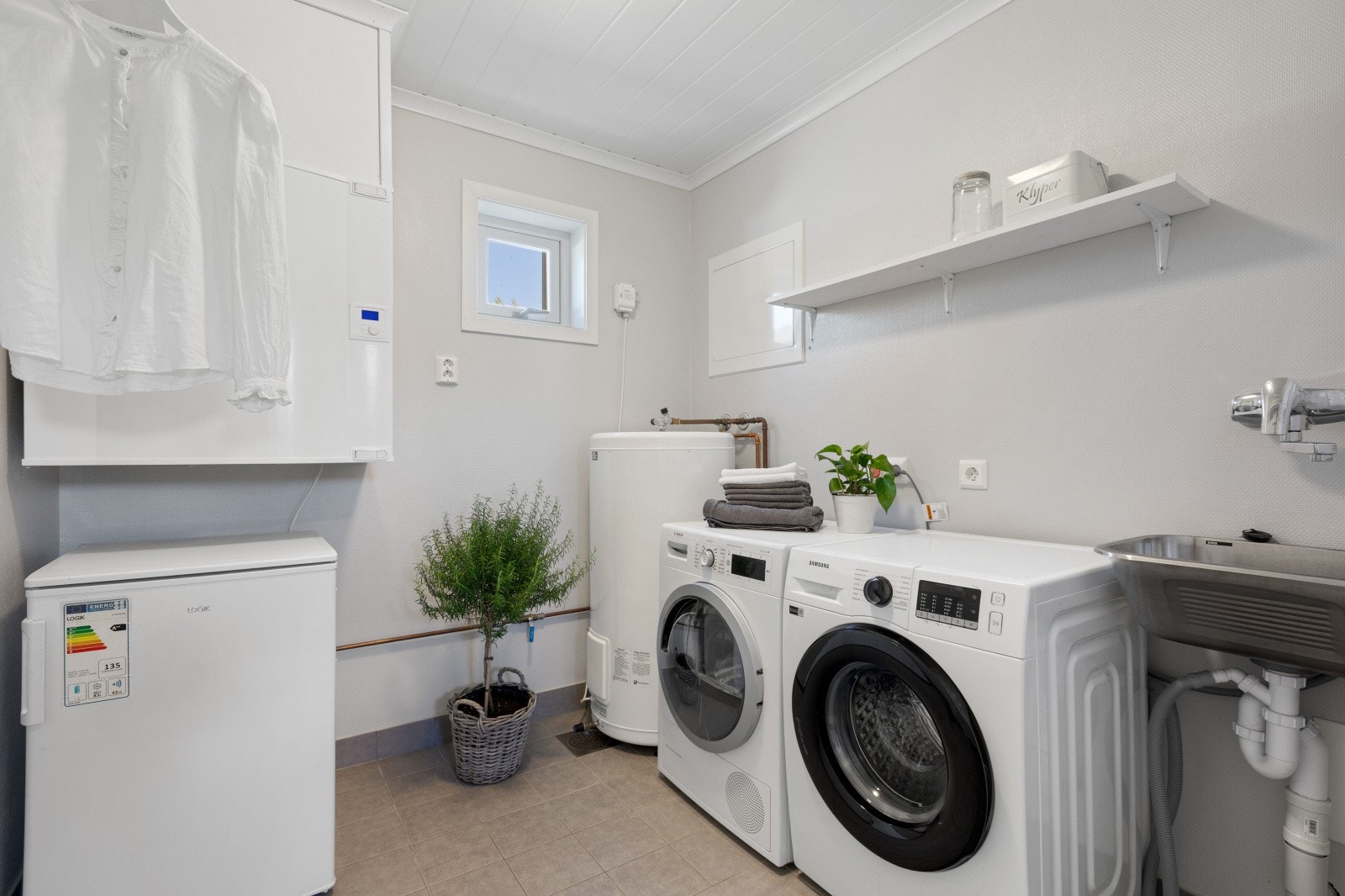 Vaskerommet har flislagt gulv med behagelig varme og er praktisk utstyrt med utslagsvask, opplegg for vaskemaskin samt varmtvannsbereder plassert her. Galleribilde