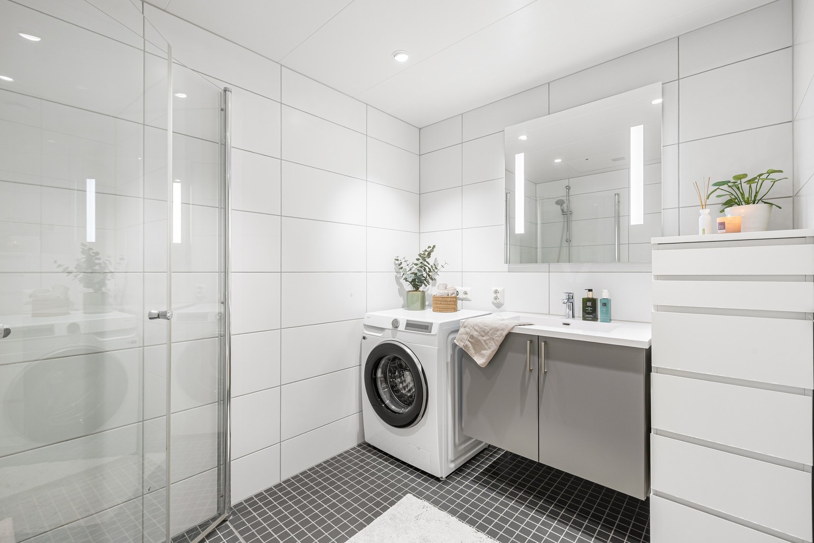 Baderommet er innredet med dusjdører i glass, veggmontert WC, dusjbatteri og garnityr montert på vegg. Legg merke til downlights i himling. Galleribilde