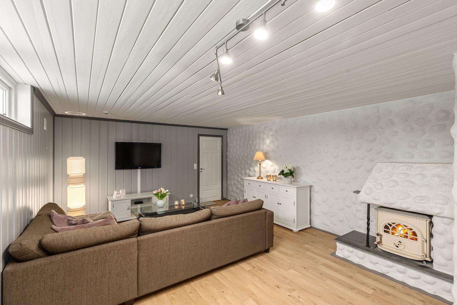 Lun og trivelig kjellerstue med god plass til sofa og samvær, stemningsskapende vedovn og en planløsning som gjør rommet lett å møblere. Galleribilde