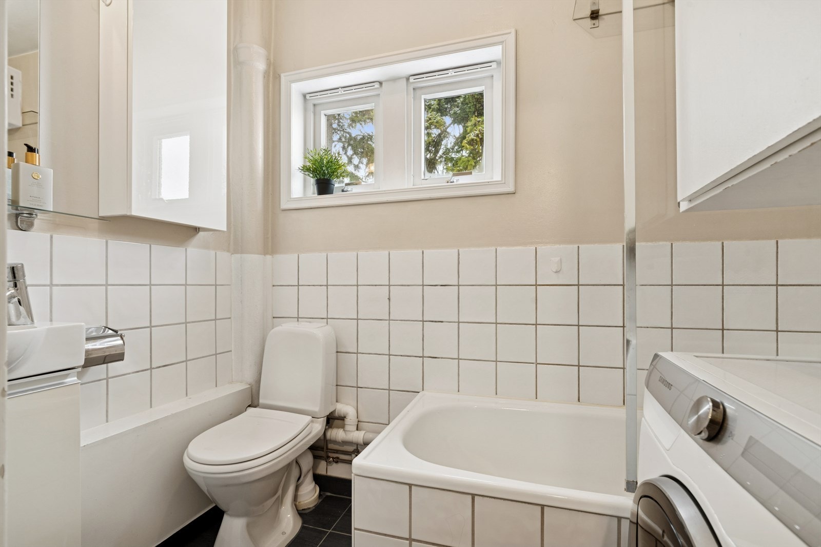 Badet er tidløst innredet med grå fliser på gulvet og en kombinasjon av hvite fliser og malte flater på vegg. Galleribilde