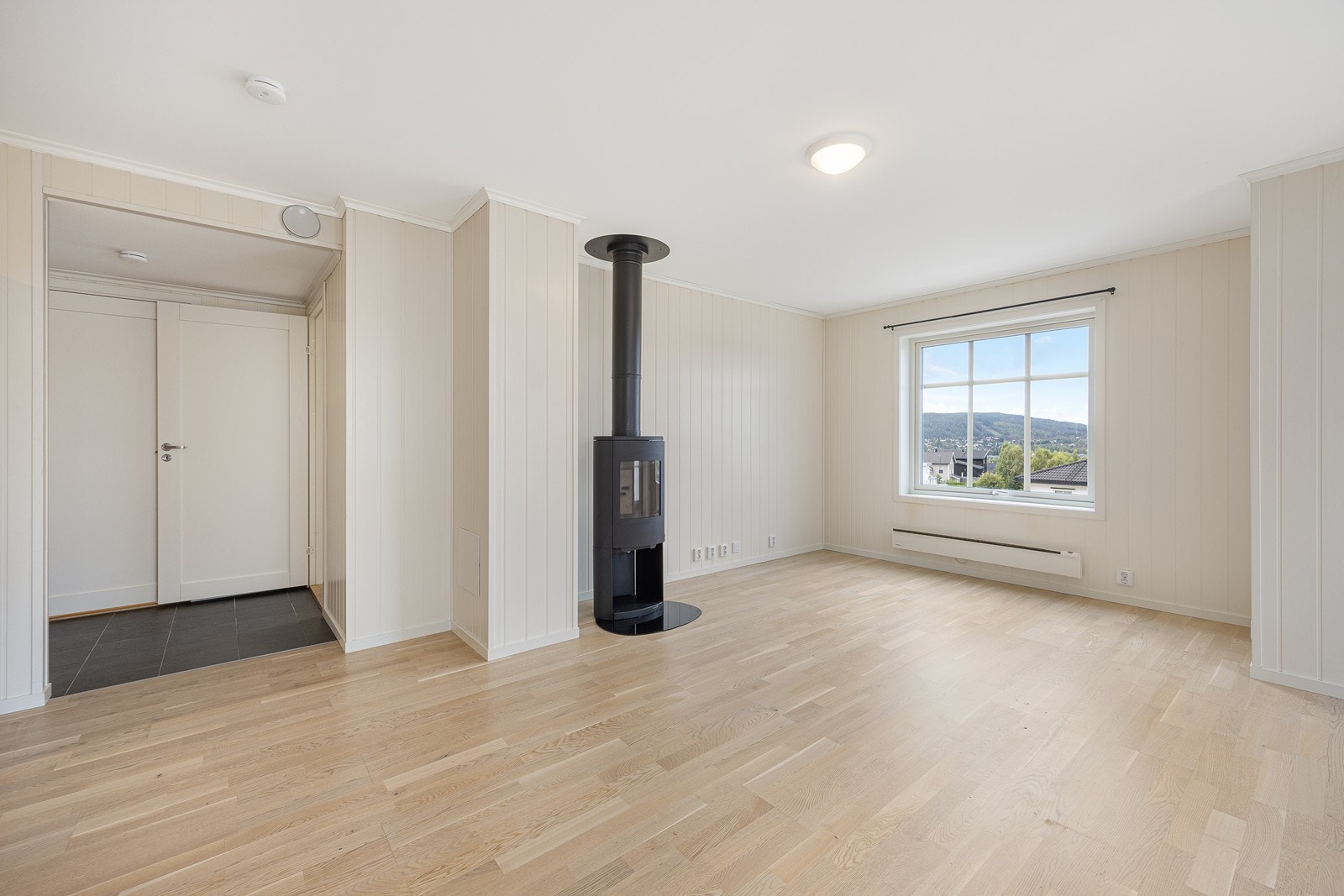 Veggene er lysmalte og står godt til det gylne parkettgulvet, og rommet inneholder en sort, moderne peisovn med stort flammebilde. Galleribilde