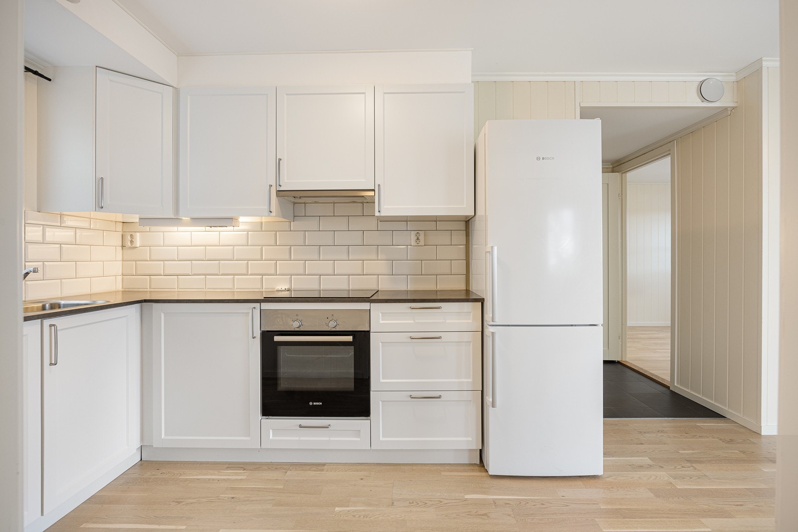 Kjøkkenet har et stilfullt og arealeffektivt design med gode benkeflater og mye oppbevaringsplass. Innredningen har hvite, profilerte fronter og koksgrå laminatbenkeplate med nedfelt vaskekum. Galleribilde