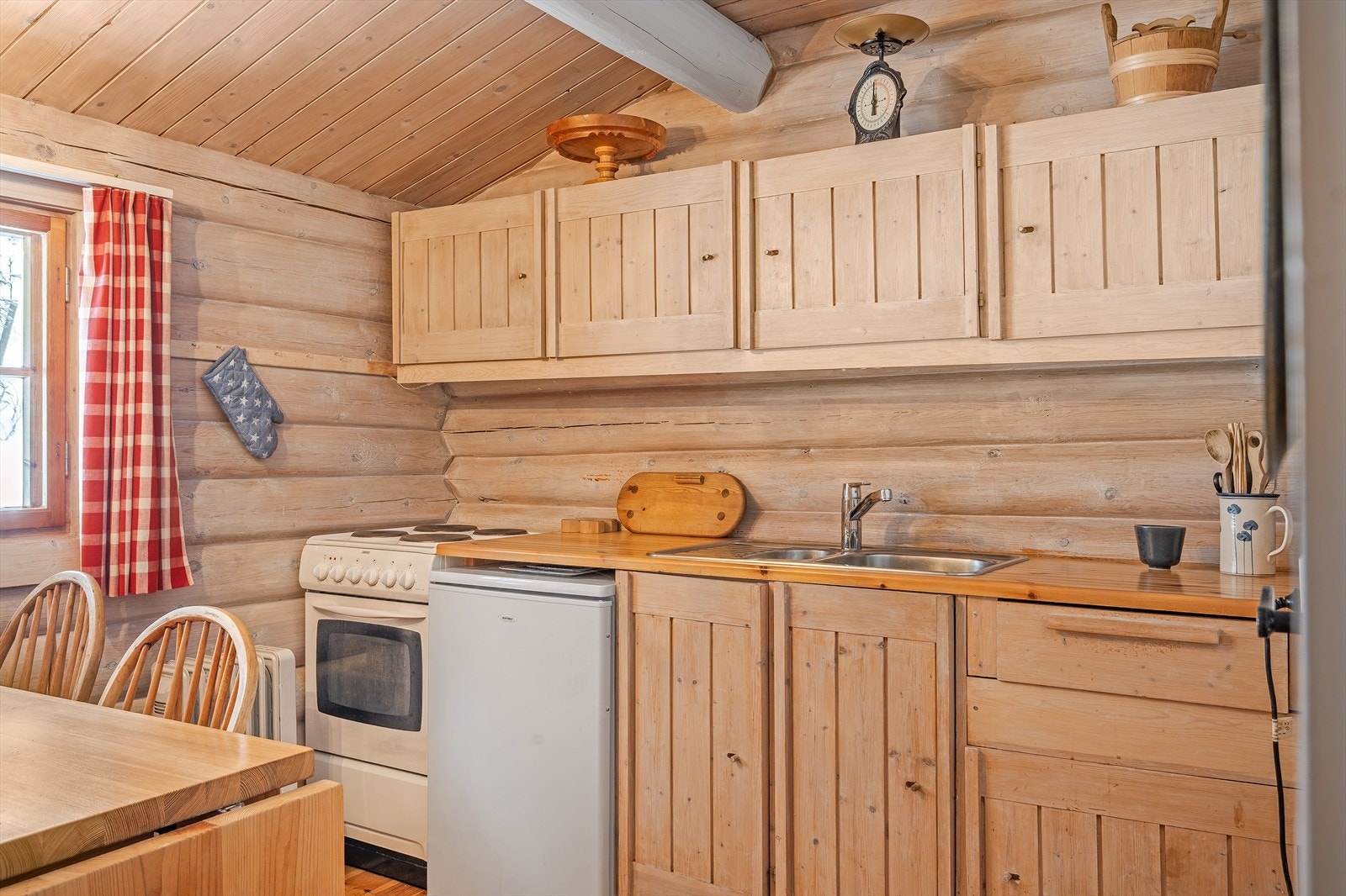 Tidstypisk kjøkken i brukspreget tilstand. Innredning med profilerte dører og heltre benkeplate. Komfyr med fire kokeplater, kjøleskap samt stålkum med ett-greps kran. Galleribilde