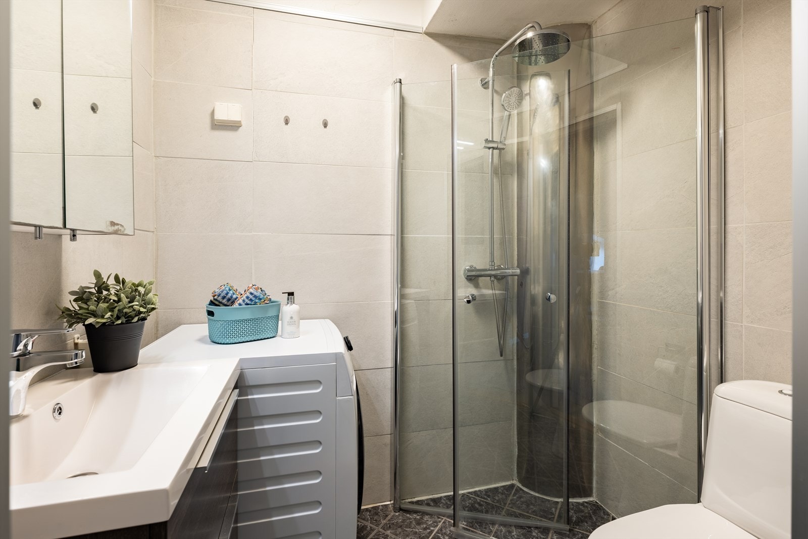 Pent flislagt baderom med dusjhjørne, opplegg til vaskemaskin, toalett, servant med underskuffer og speilskap. Galleribilde