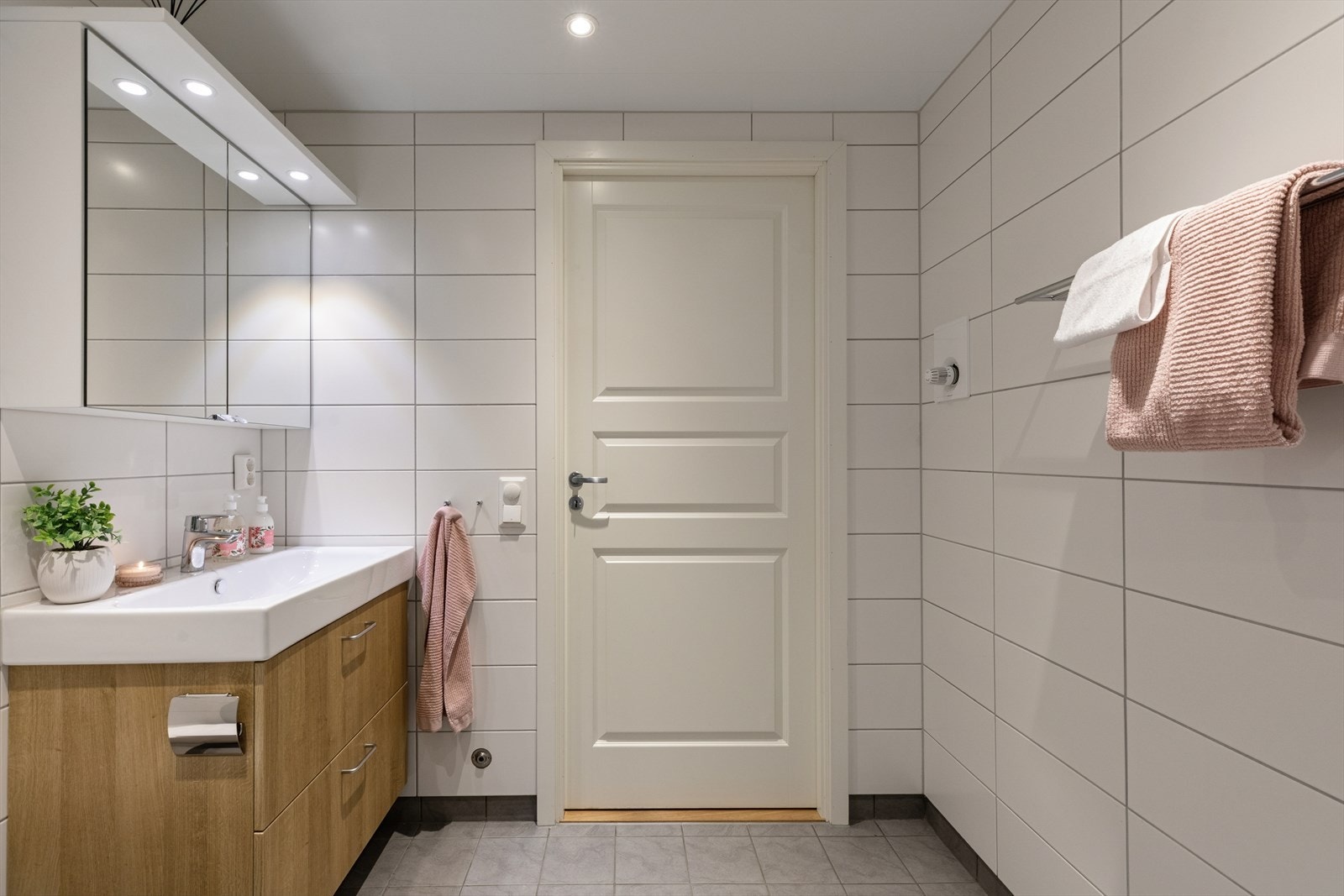 Badet er innredet med nedfelt servant, speilhylle med belysning, veggmontert toalett med innebygd sisterene, dusjhjørne med dører i herdet glass. Galleribilde