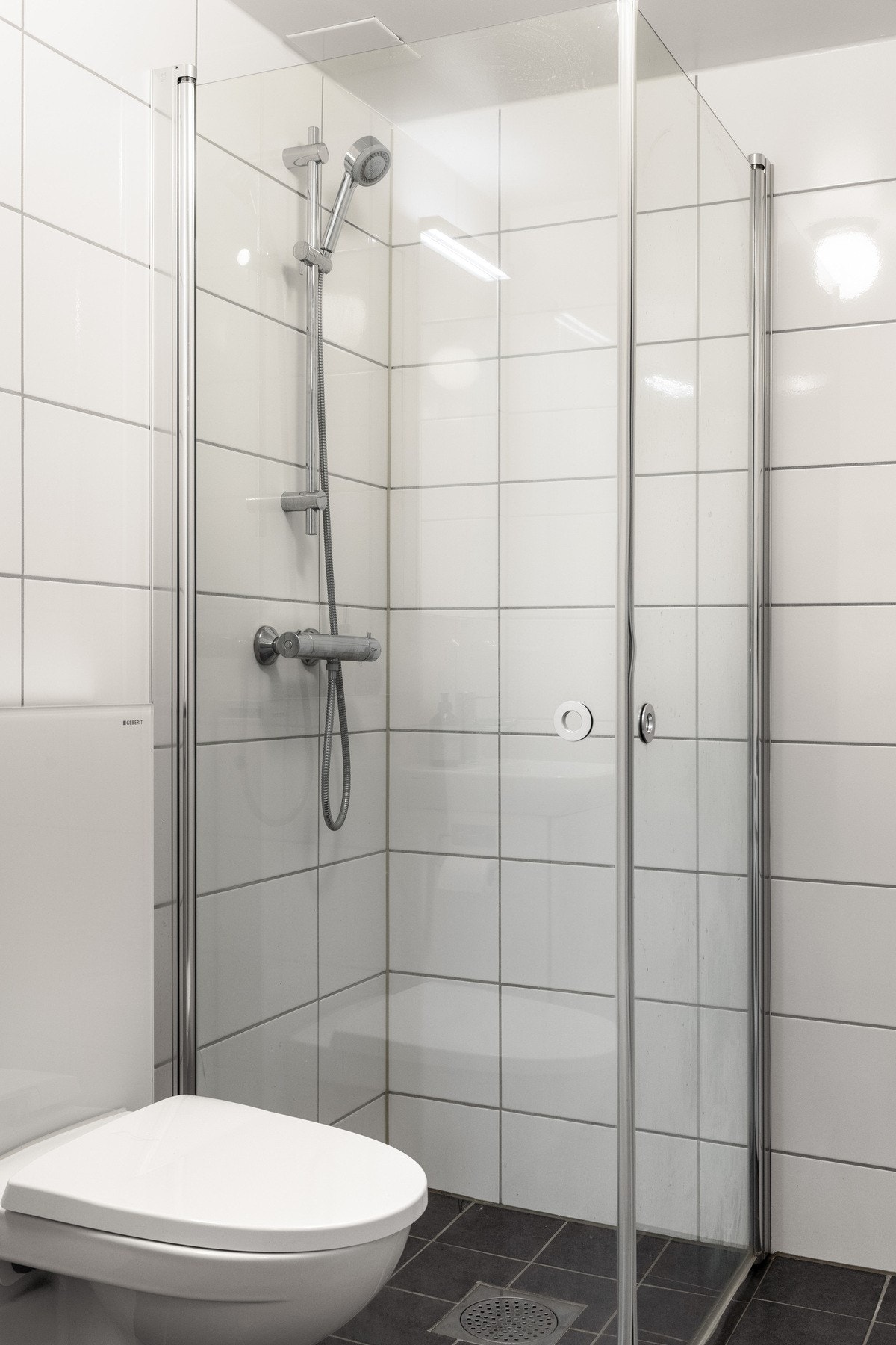 Dusjhjørne med dører og vegghengt toalett med innkasset sisterne gir et plassbesparende uttrykk. Galleribilde