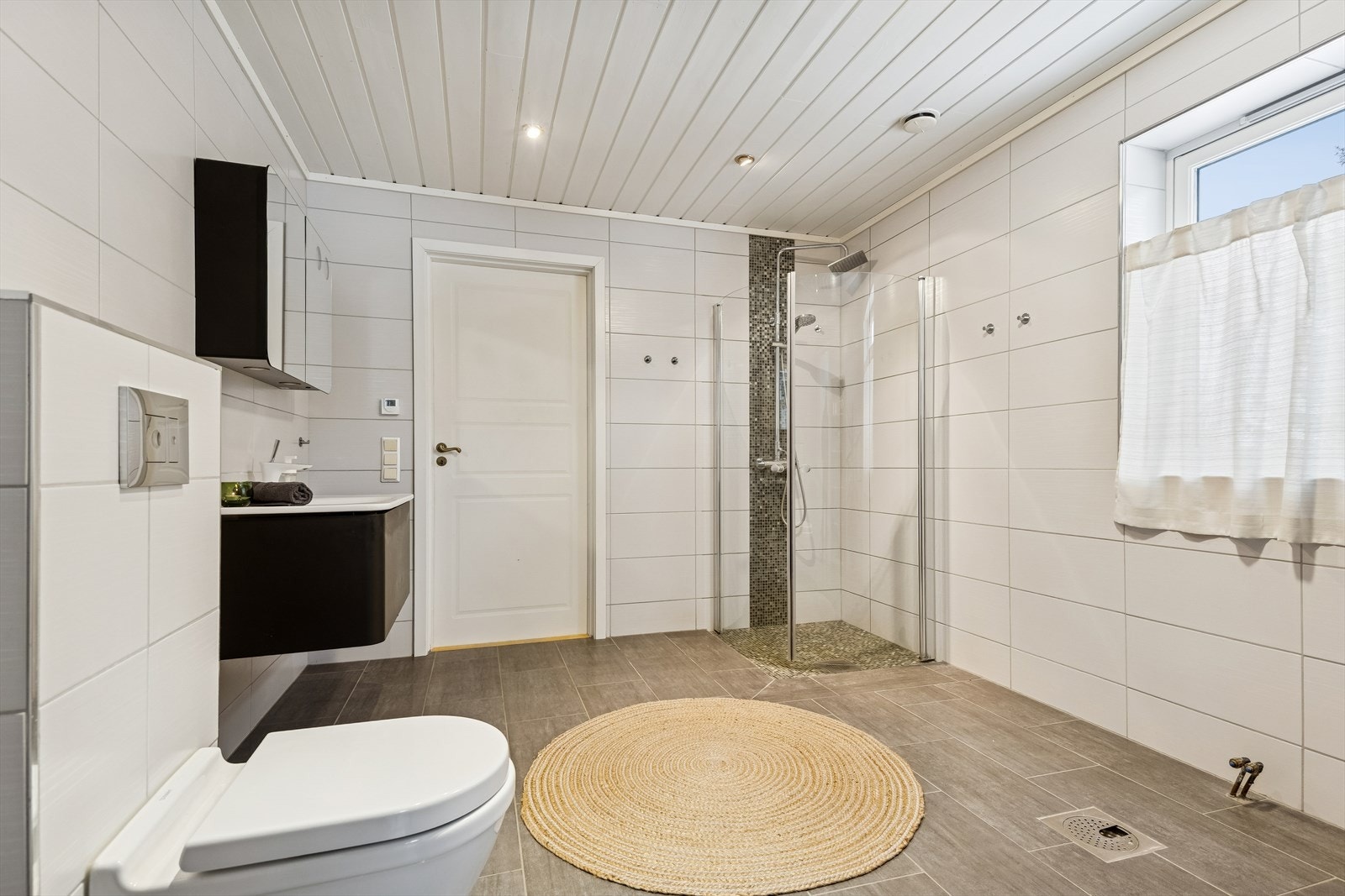 Flislagt bad med vegghengt toalett, dusjhjørne og vannbåren gulvvarme. Galleribilde