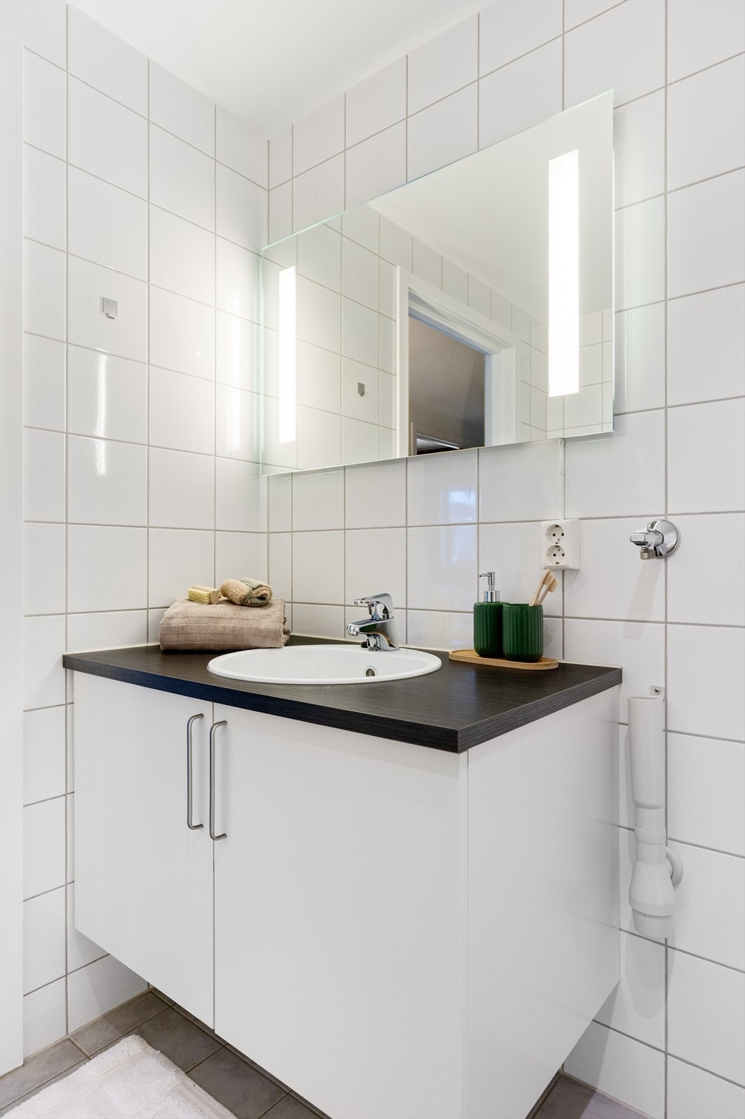 Det er god plass til oppbevaring av baderomsartikler i servantskap. Øvrig innredning består av speil med integrert belysning, en praktisk og åpen dusjløsning, vegghengt toalett og opplegg for vaskemaskin. Galleribilde