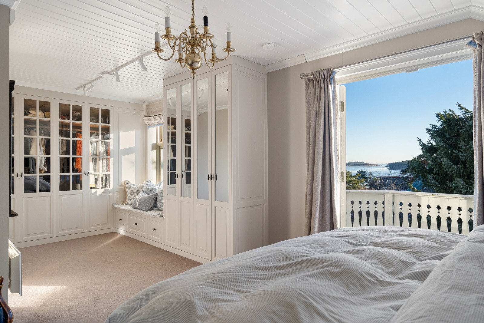 Åpent walk-in closet har glass- og speilskap i en L form med sittebenk. Galleribilde