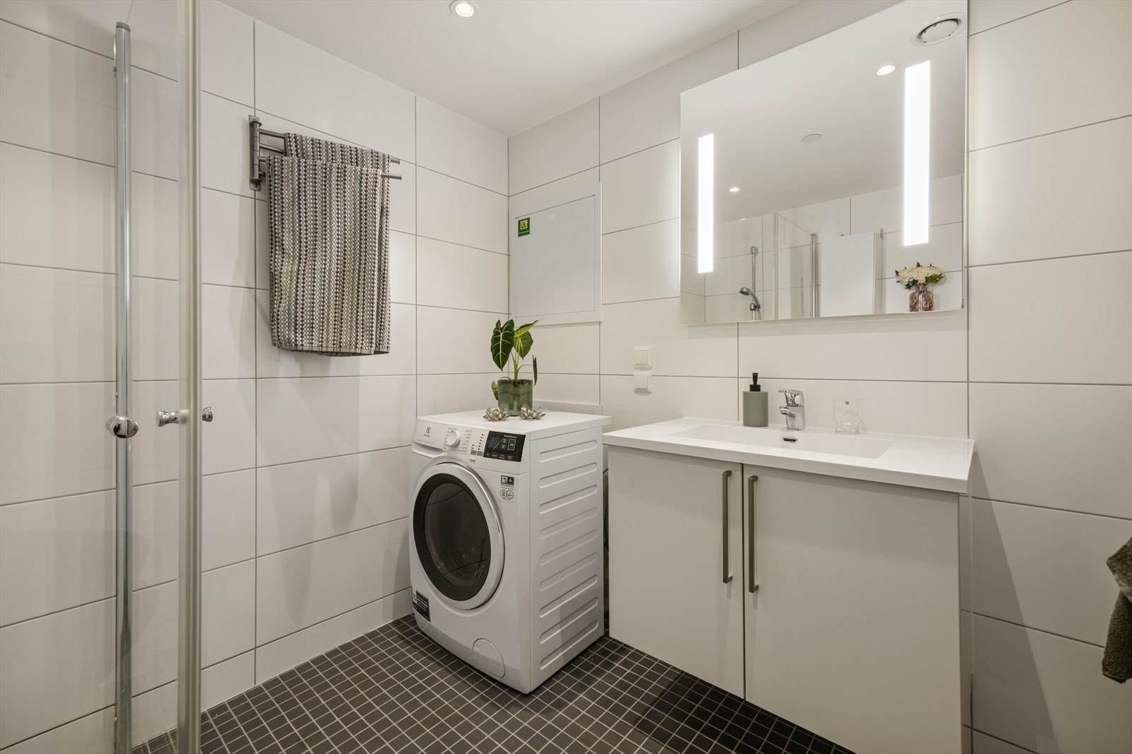 Rommet er innredet med dusjvegger av glass og dusjgarnityr på vegg, vegghengt toalett, innredning med servant og opplegg for vaskemaskin. Galleribilde