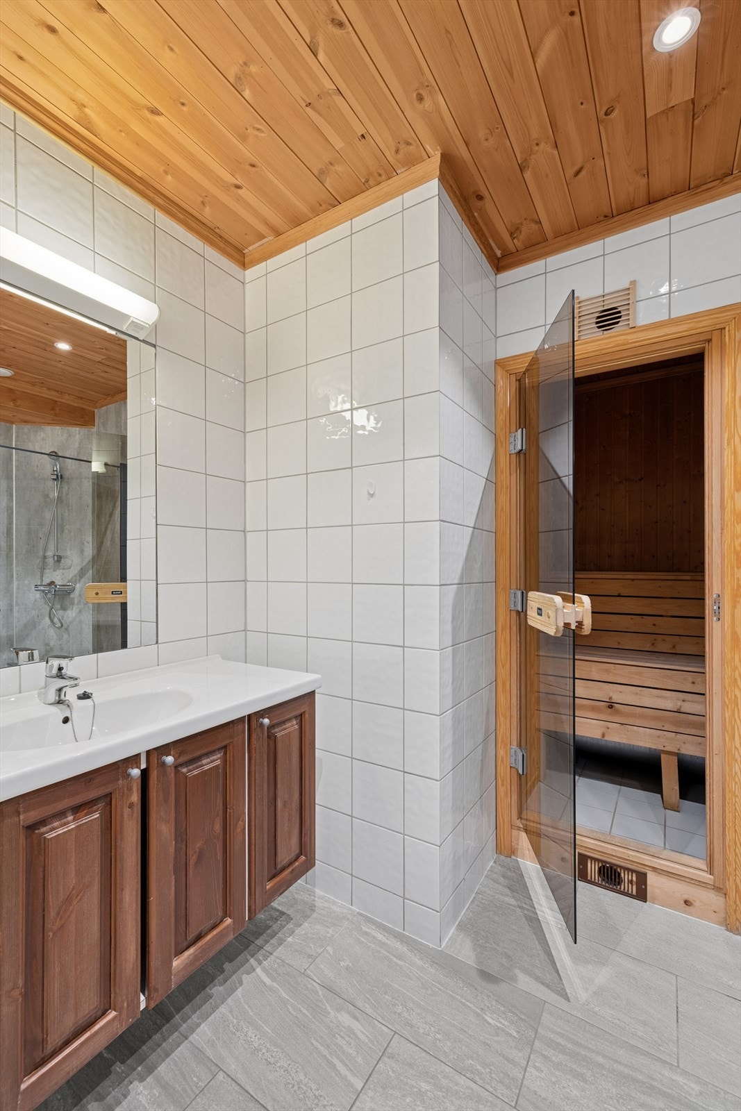 Badet inneholder gulvstående toalett, dusjhjørne og servantinnredning med skap. Over servanten er det speil og belysning. Galleribilde