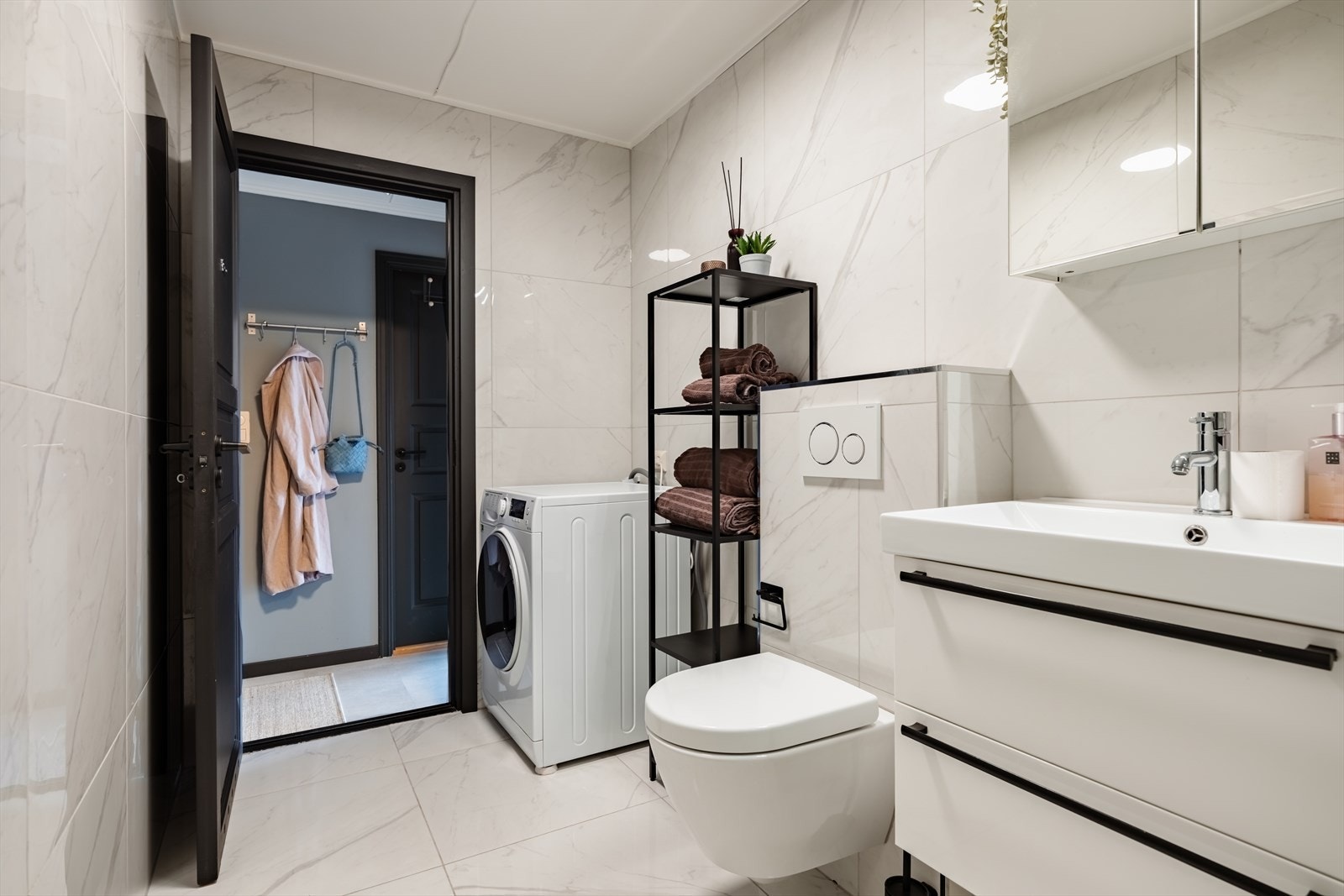 Delikat bad med vegghengt toalett, servant med skuffer og praktisk opplegg for vaskemaskin. Galleribilde