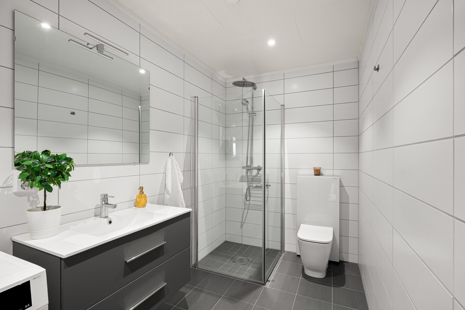 Innredningen består av servant med underskap og speil med belysning, samt dusjhjørne med glassdører og vegghengt toalett. Galleribilde