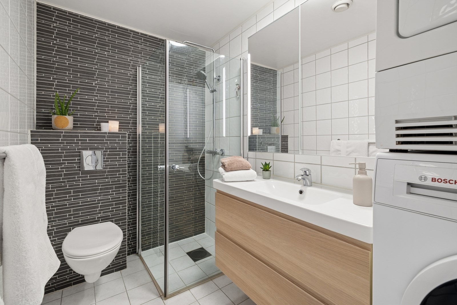 Pent baderom i hovedetasjen med dusjhjørne med innfellbare dører, vegghengt WC med innbygget sisterne, servant med underskuffer og speilskap med belysning. Opplegg for vaskemaskin og tørketrommel. Galleribilde