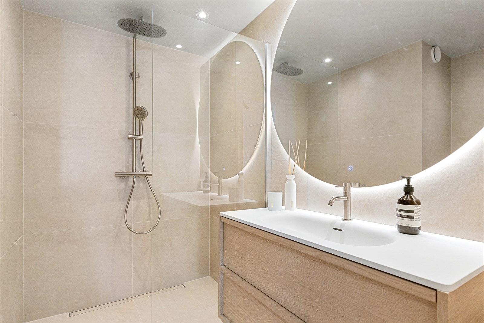 Baderomsinnredning med eikemønster og matt, helstøp benkeplate med nedsenket servant. Stor dusjsone med fast glassvegg, regnfallsdusj og designsluk fra Purus Line i langs vegg - en detalj som både er funksjonell og estetisk Galleribilde