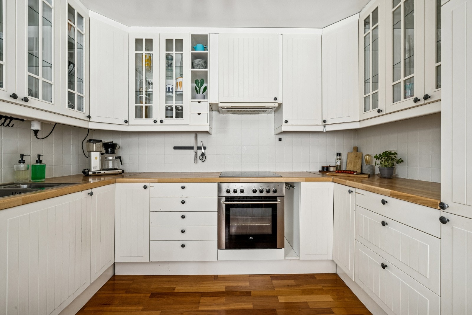 IKEA kjøkkeninnredning med glatte fabrikklakkerte skapfronter, laminert benkeplate med fliser på bakvegg, 1 1/2 oppvaskkum, ventilator og innfelte hvitevarer som koketopp, stekeovn, oppvaskmaskin, kjøl/- fryseskap. Galleribilde