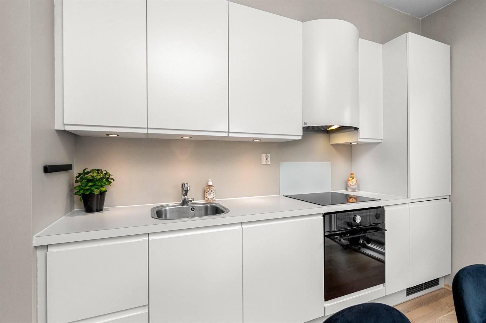 Kjøkkenet strekker seg langs den ene veggen og byr på godt med skap- og benkeplass. Her har du tidløs utforming med hvite og håndtaksfrie fronter og lys benkeplate. Galleribilde