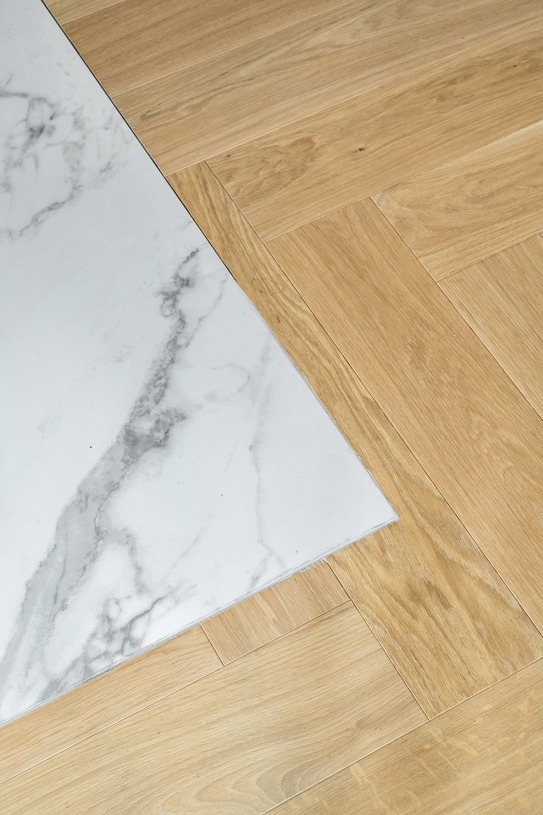 Detaljbilde som fremhever de gjennomførte materialvalgene i boligen. Den nydelige fiskebeinsparketten møter lyse, steinpregede fliser og skaper en stilren kontrast mellom varme og kjølige toner. Galleribilde