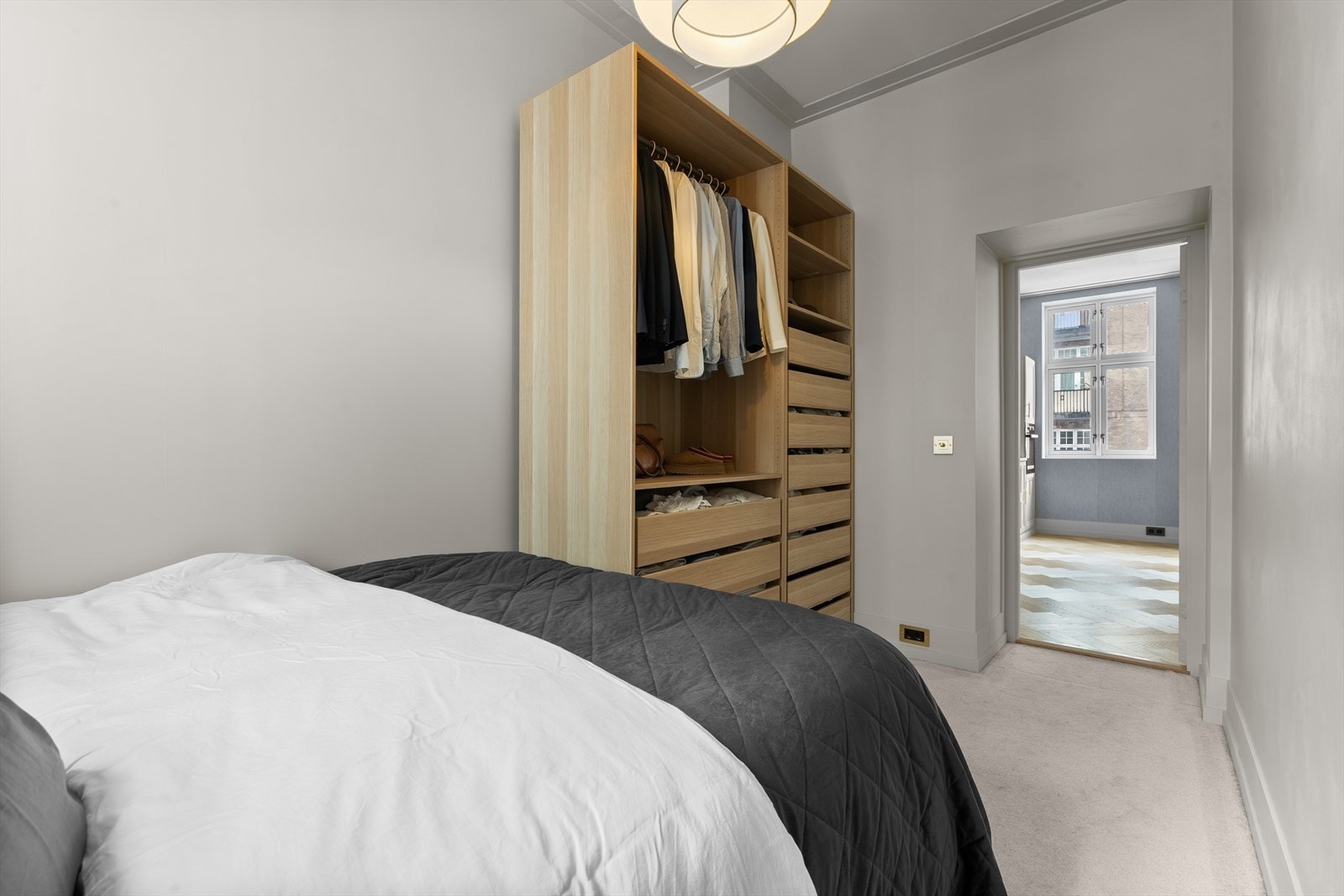 Gulvet er belagt med et lyst og komfortabelt vegg-til-vegg-teppe som tilfører ekstra varme og demper romklangen. Oppbevaringsbehovet ivaretas av et romslig, åpent PAX-garderobeskap med gode organiseringsmuligheter og enkel oversikt over garderoben. Galleribilde