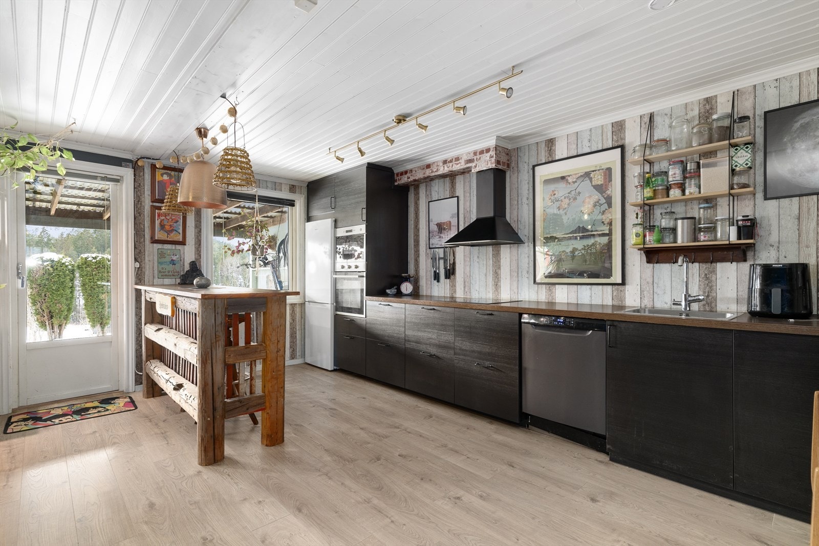 Langs den ene veggen er det et stilig og moderne kjøkken fra IKEA i mørk utførelse fra 2018. Kjøkkenet har et lett og avslappet uttrykk, med mye åpen veggplass i stedet for overskap. Galleribilde