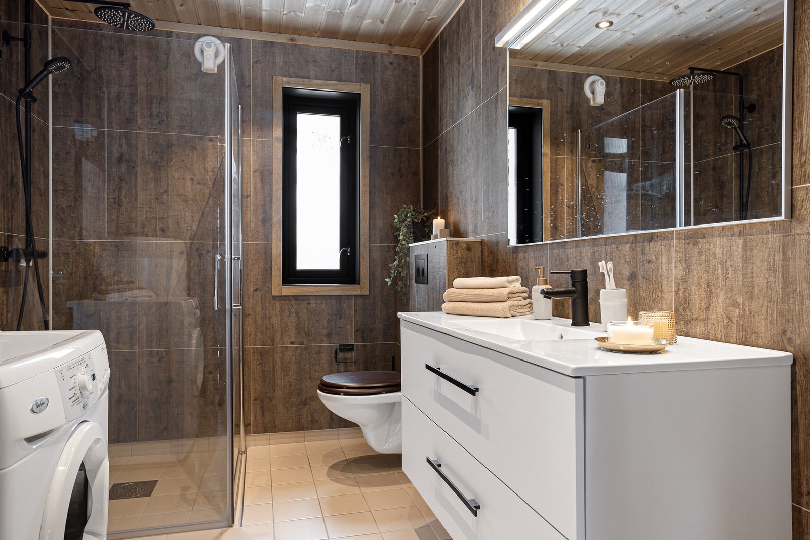 Smakfullt innredet bad som er innredet med toalett, dusjnisje med glassdører, baderomsinnredning med servant og speil over, samt opplegg for vaskemaskin Galleribilde