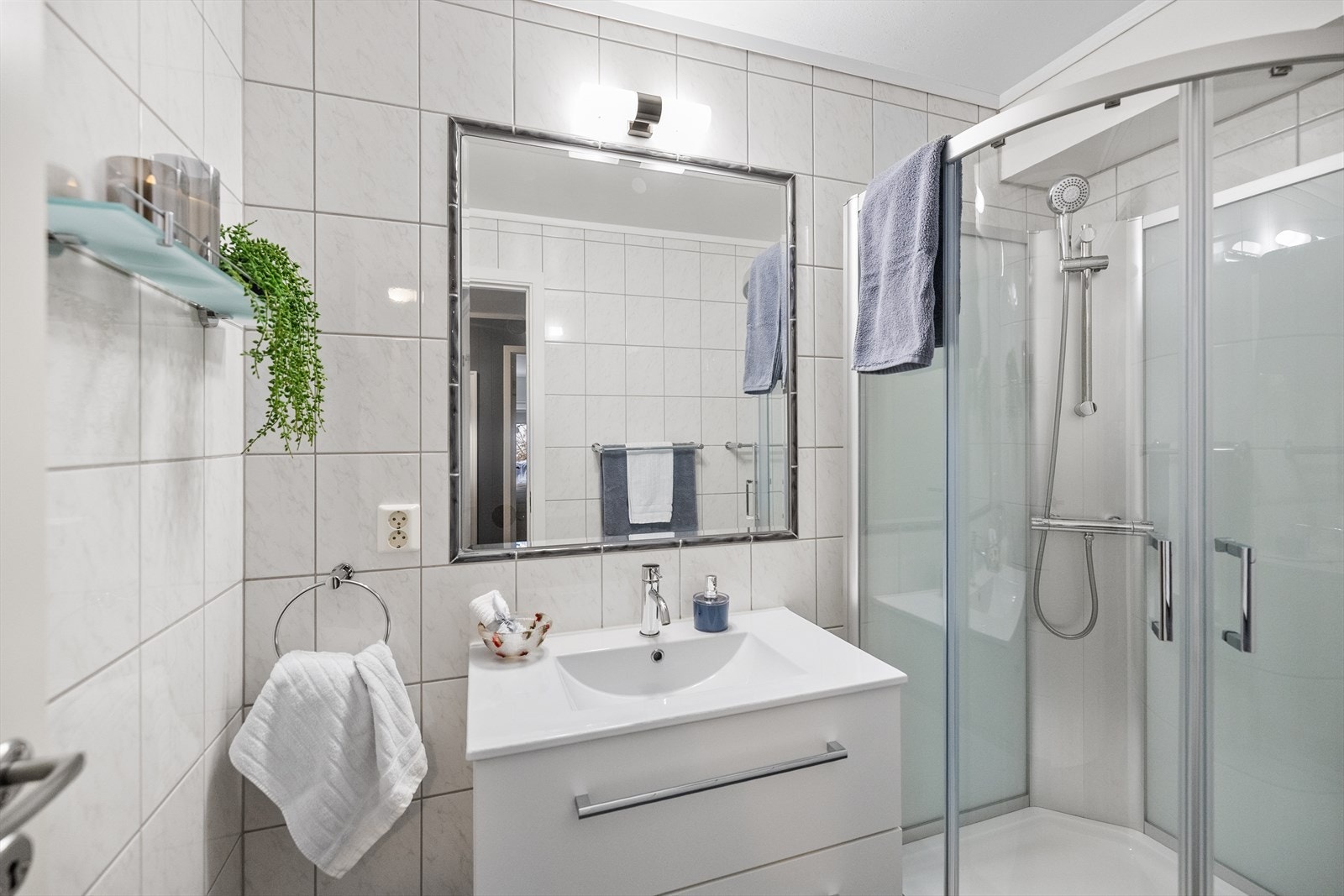 Baderommet fremstår som pent og funksjonelt, med flislagt gulv utstyrt med varmekabler som gir god komfort året rundt. Veggene er flislagt, noe som gir rommet et tidløst og lettstelt uttrykk, mens taket i malt betong gir en moderne og robust finish. Galleribilde