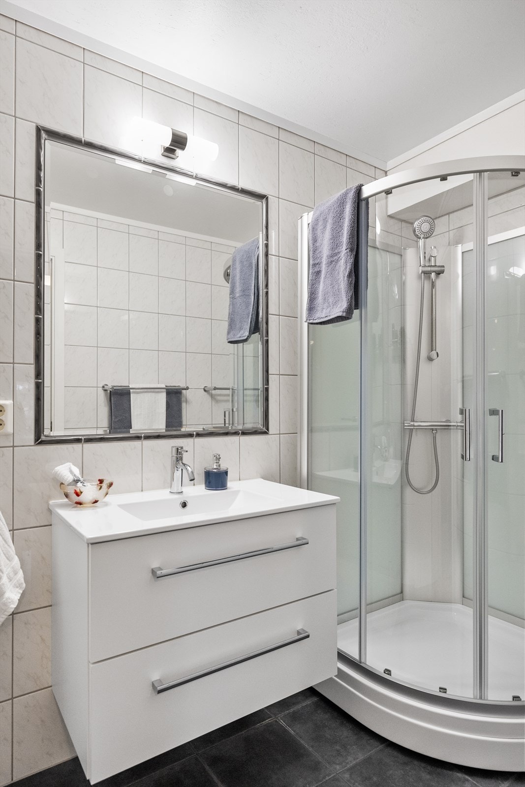 Baderommet er innredet med nedfelt servant med tilhørende innredning, som gir både praktisk oppbevaring og et ryddig uttrykk. Dusjkabinett sørger for en praktisk dusjløsning og bidrar til enkel rengjøring. Galleribilde
