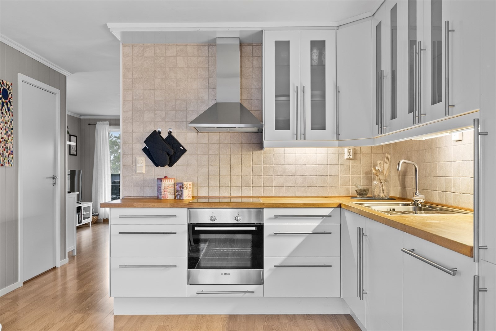 Kjøkkeninnredningen har glatte fronter i lyse toner som understreker det moderne uttrykket. Benkeplatene i laminert heltre tilfører varme og karakter, samtidig som de gir rikelig med arbeidsflate. Galleribilde