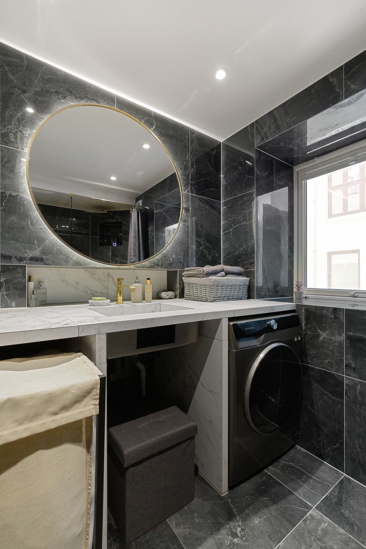 Badet har lekre detaljer med mørke fliser, lys benkeplate i marmor-utførelse, samt rundt speil med bakbelysning som gir et sofistikert uttrykk. Galleribilde