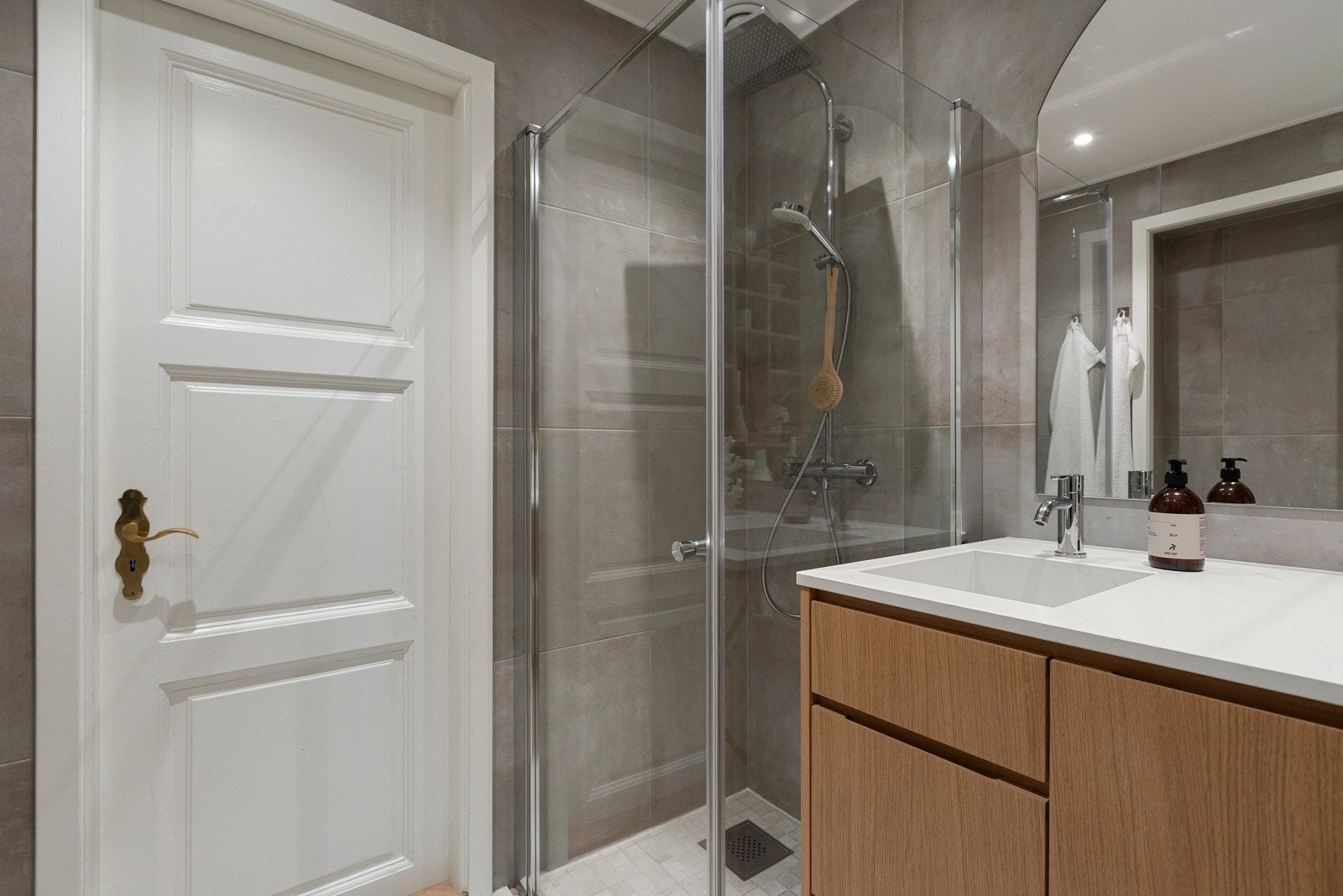 Badet er innredet med veggmontert toalett, dusjnisje, stort veggspeil og servant nedfelt i servant med innredning med skuffer og skap. Galleribilde