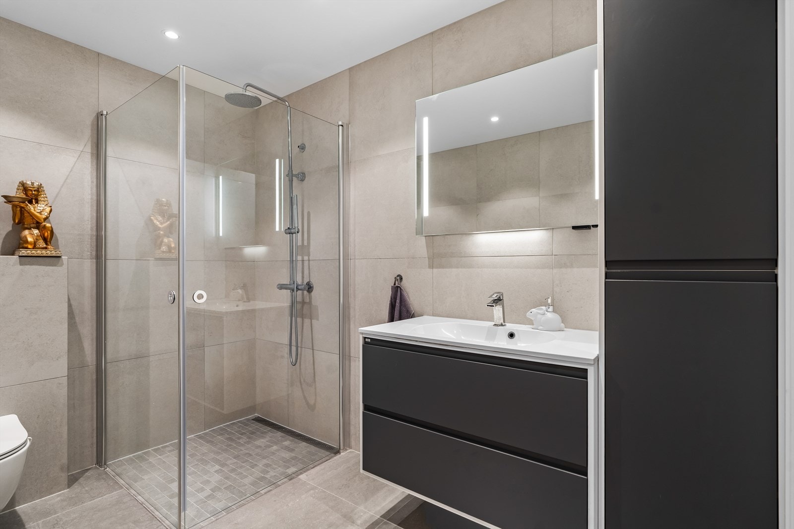 Rommet er utstyrt med innfellbare dusjdører, mekanisk avtrekk, servantskap og veggmontert wc. Galleribilde