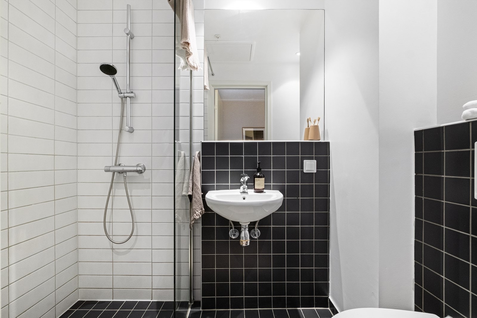 Baderom med flislagt gulv, varmekabler, fliser og malte flater på vegger, avtrekk, speil, downlights, servant, dusj hjørne med glassvegg, vegghengt toalett. Galleribilde