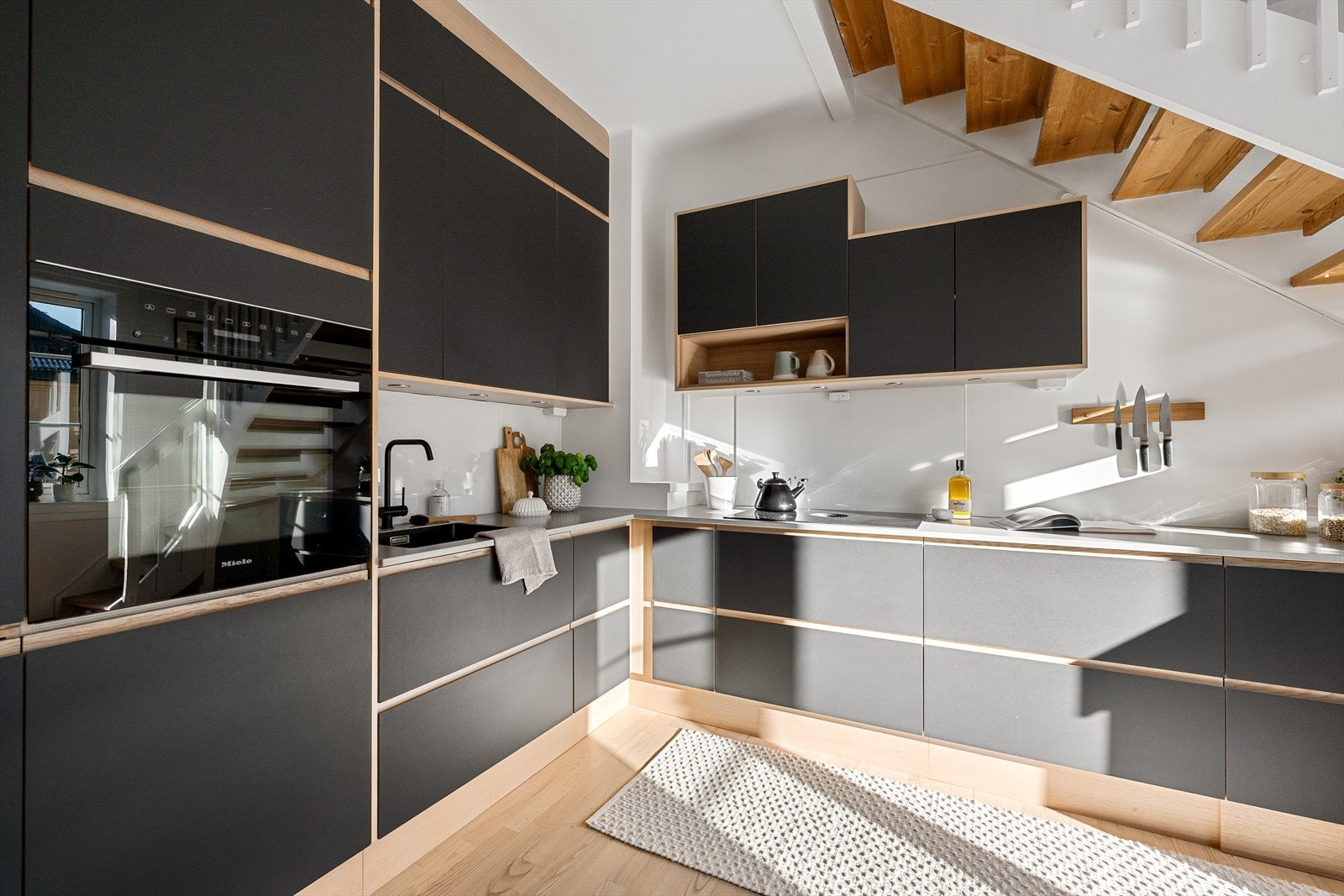 Glatt laminert kjøkkeninnredning med plater mellom overskap og kompositt benkeplate. Kum med ettgreps blandebatteri, kullfiltervifte integrert i koketopp, integrert ovn, kjøl/frys og oppvaskmaskin, samt lys under overskap. Galleribilde