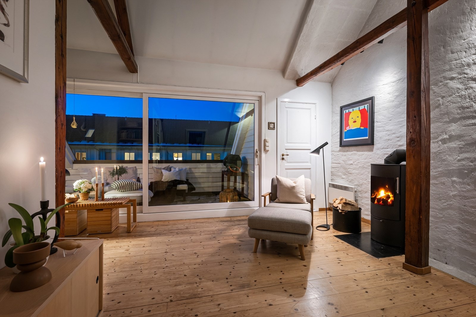 Loftstuen samler peis, originale tregulv og synlige bjelker mot murvegg - arkitektoniske detaljer som gir rommet særpreg og en lun atmosfære med takterrassen rett utenfor. Galleribilde