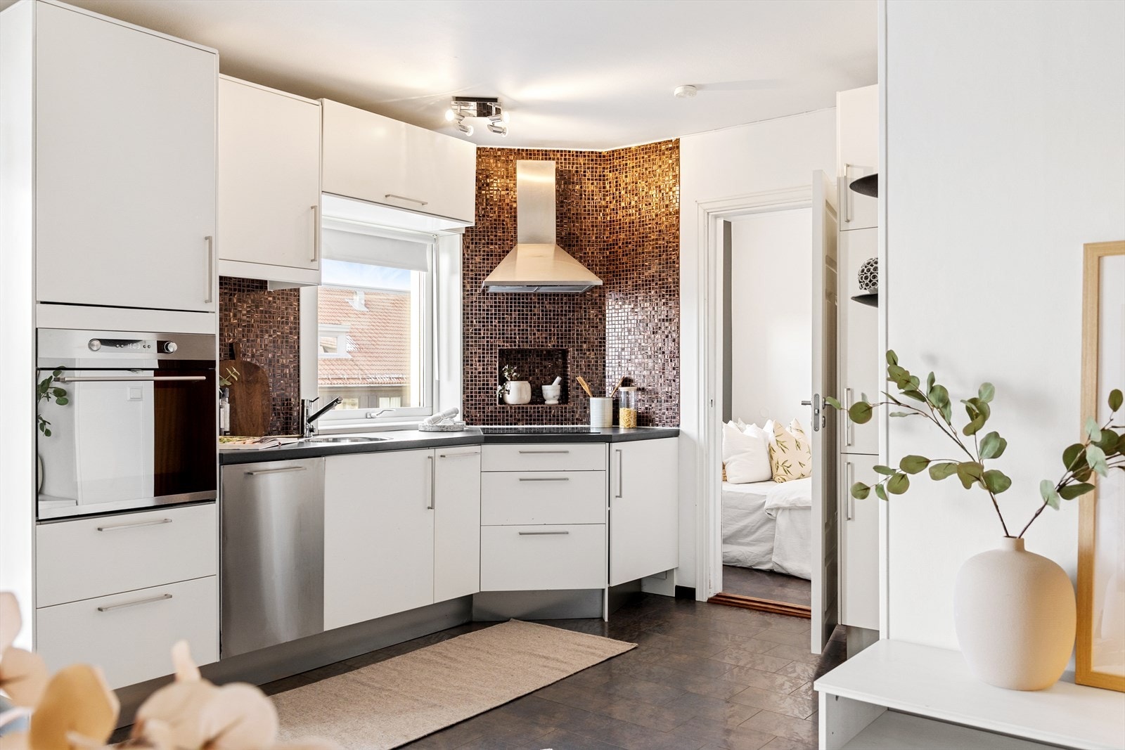 Kjøkkeninnredningen har hvite, glatte fronter og består av høyskap samt over- og underskap, med fliser mellom benkeplate og overskap. Galleribilde