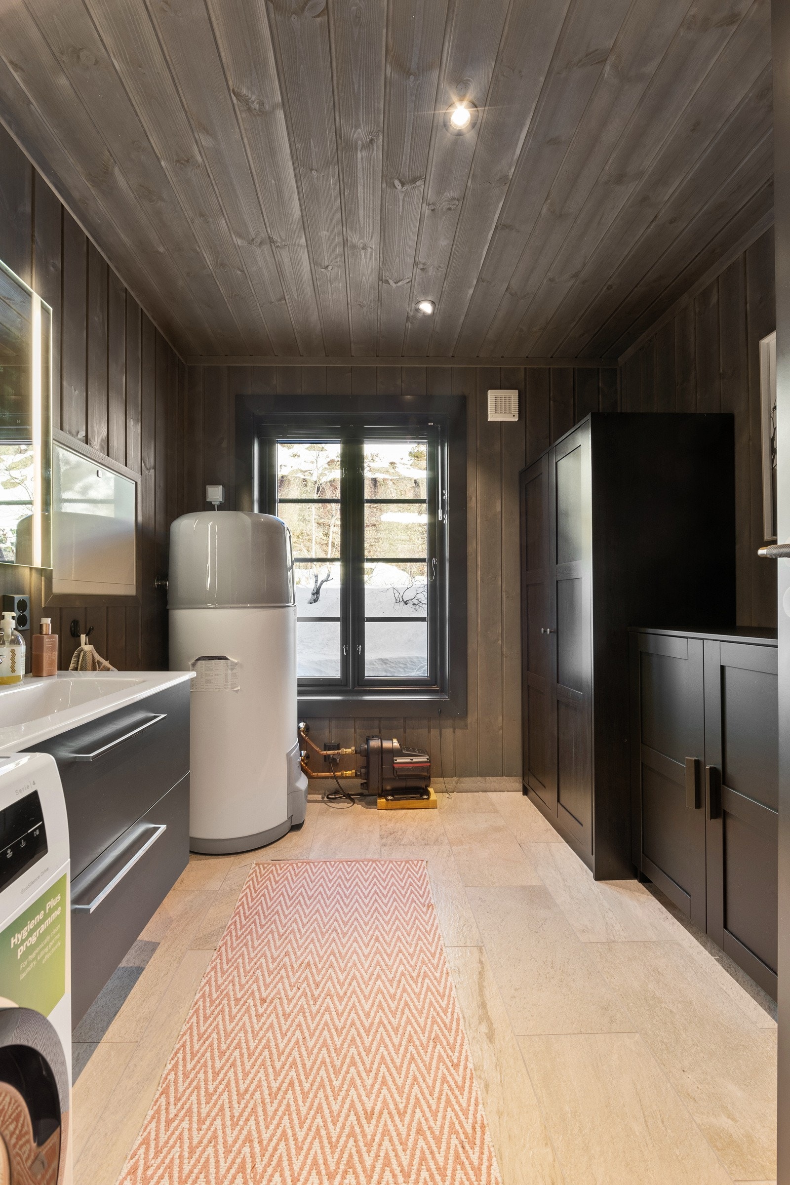 Vaskerommet har flislagt gulv og panel på vegger og i himling, som gir et helhetlig og praktisk uttrykk. Rommet er funksjonelt innredet med opplegg for vaskemaskin, varmtvannstank, servant med innredning samt toalett, og har gode arbeids- og oppbevaringsm Galleribilde