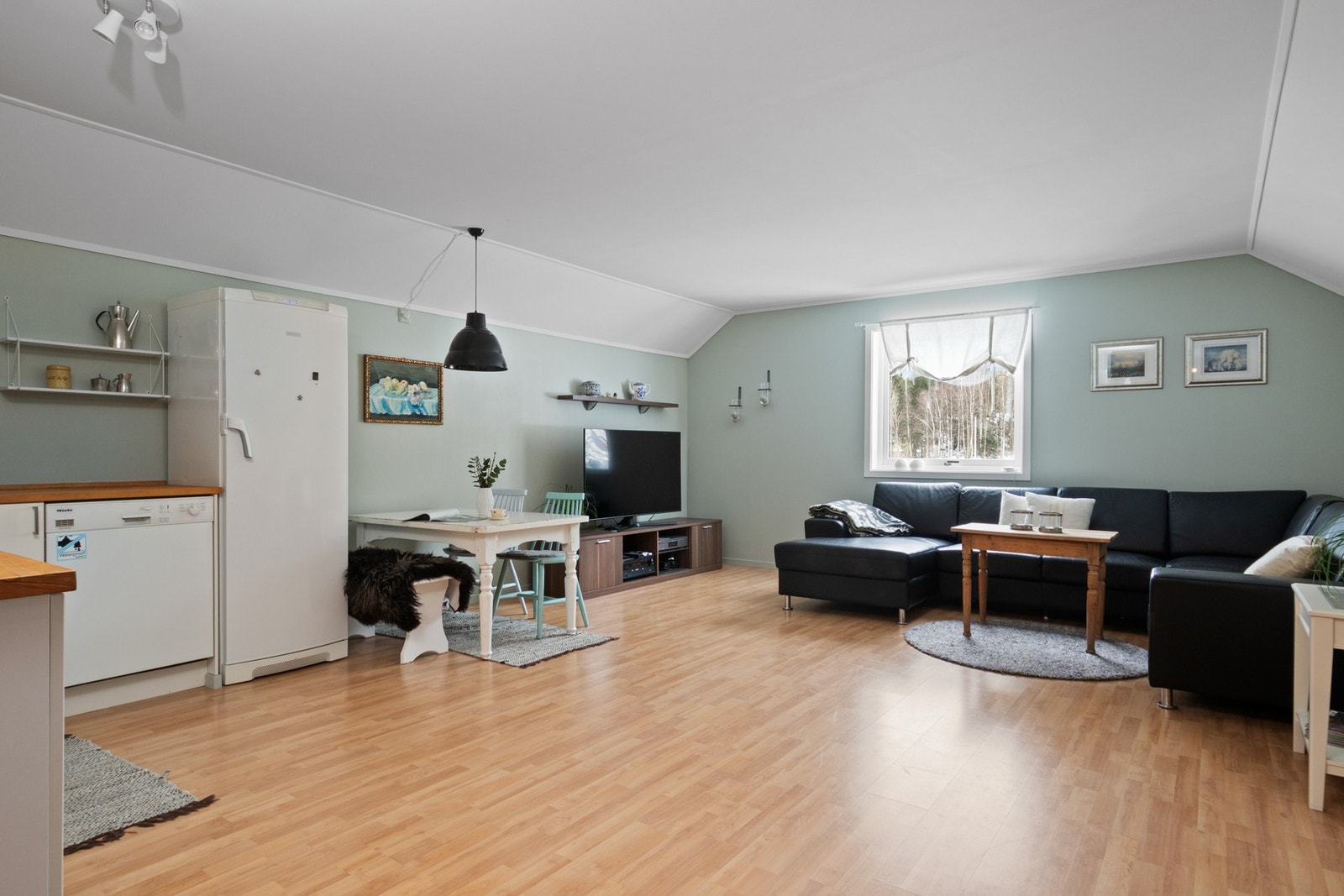 Stue og kjøkken ligger i åpen løsning, med laminatgulv og vegger malt i mintgrønn fargetone. Galleribilde