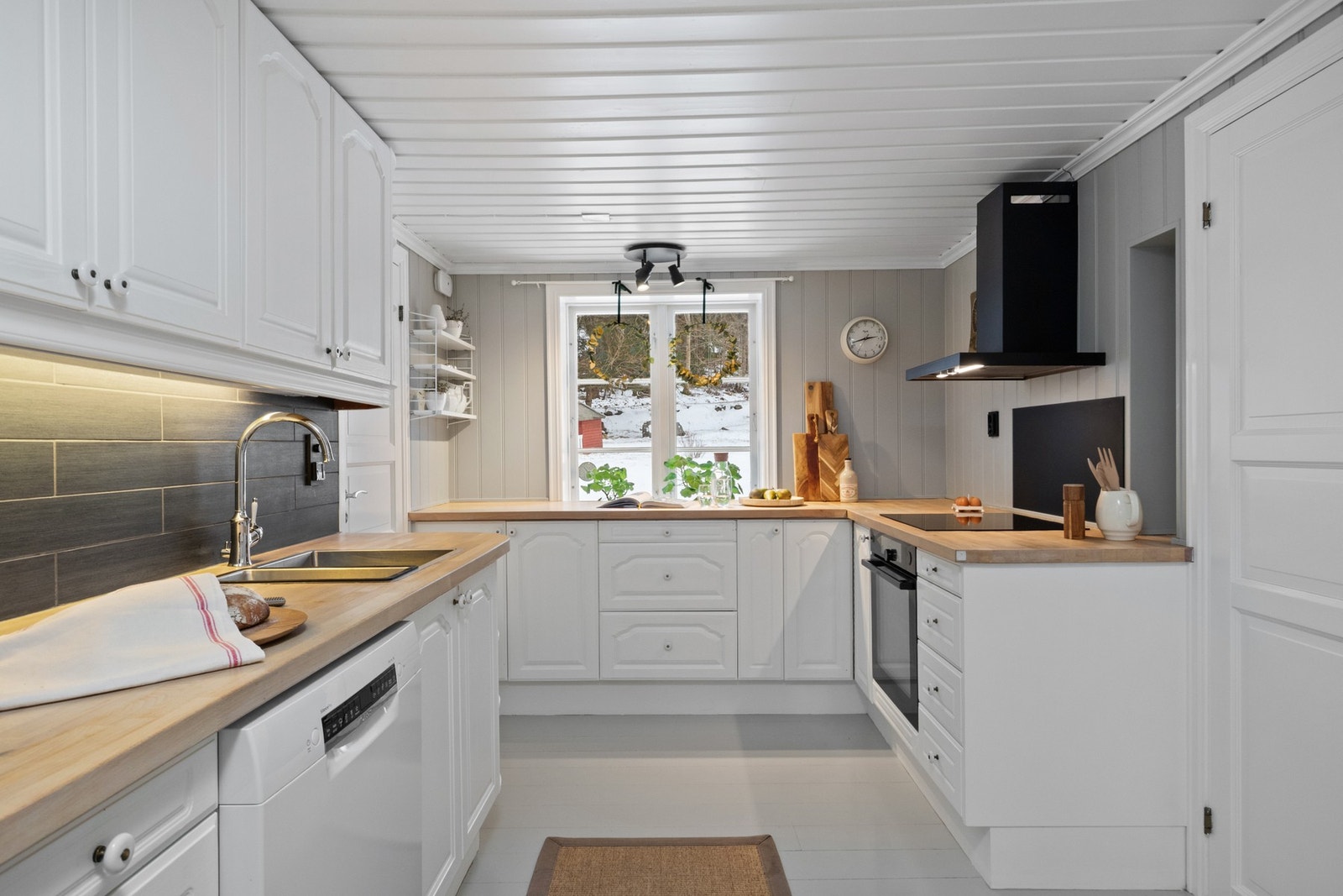 Innredningen har hvite, profilerte fronter, vinhyller, laminert benkeplate og dobbel oppvaskkum i rustfritt stål. Galleribilde