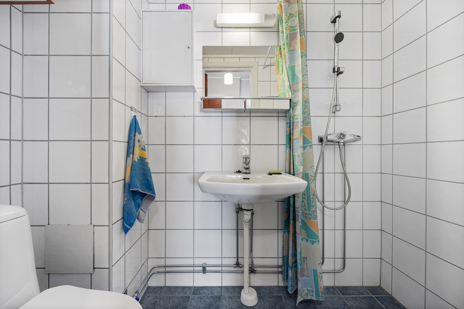 Badet er innredet med vegghengt toalett, servant med overskap og speil. Galleribilde