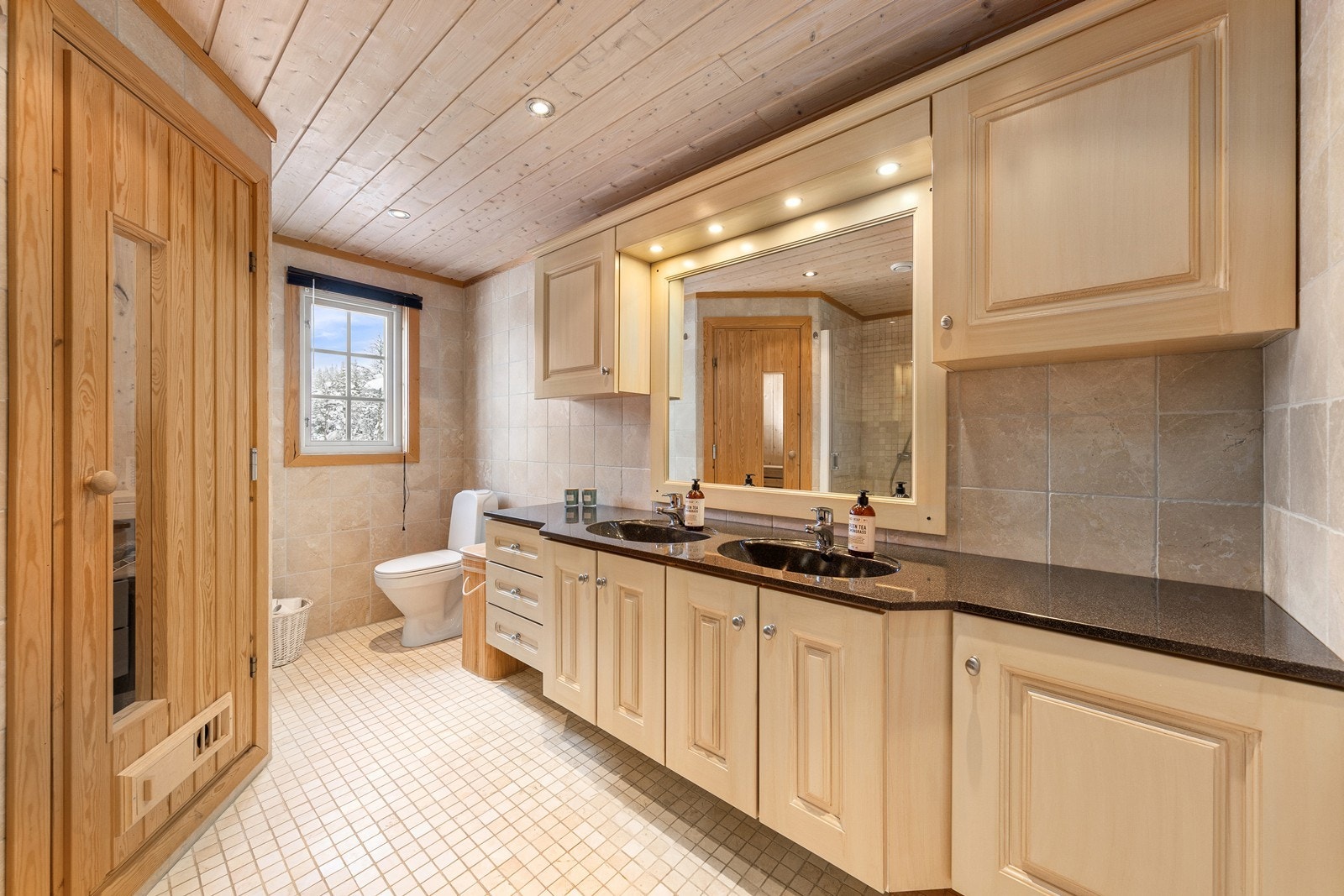 Bad med flislagte overflater, stor innredning med dobbel nedfelt servant, gulvmontert toalett, dusjnisje og badstue. Galleribilde