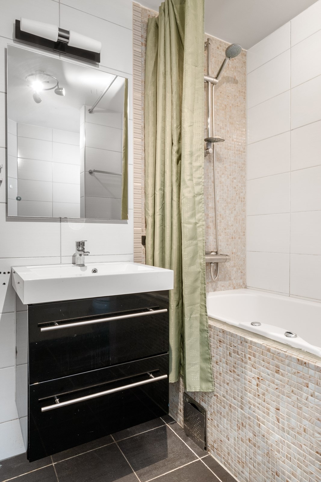 Det er innredet med et servantskap med servant som har vannuttak til vaskemaskin, et vegghengt toalett og et innfliset badekar med vegghengt dusj. Galleribilde