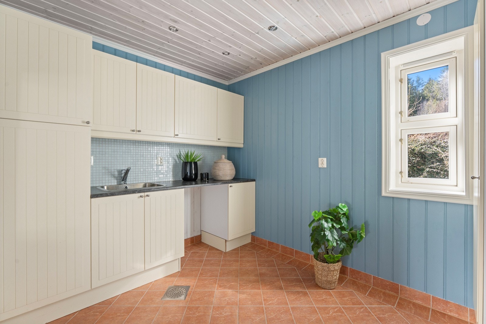 Praktisk vaskerom med panel på vegger og flislagt gulv med både elektriske varmekabler og vannbåren gulvvarme. Rommet er utstyrt med opplegg for vaskemaskin, underskap med skyllekum og god skapplass Galleribilde