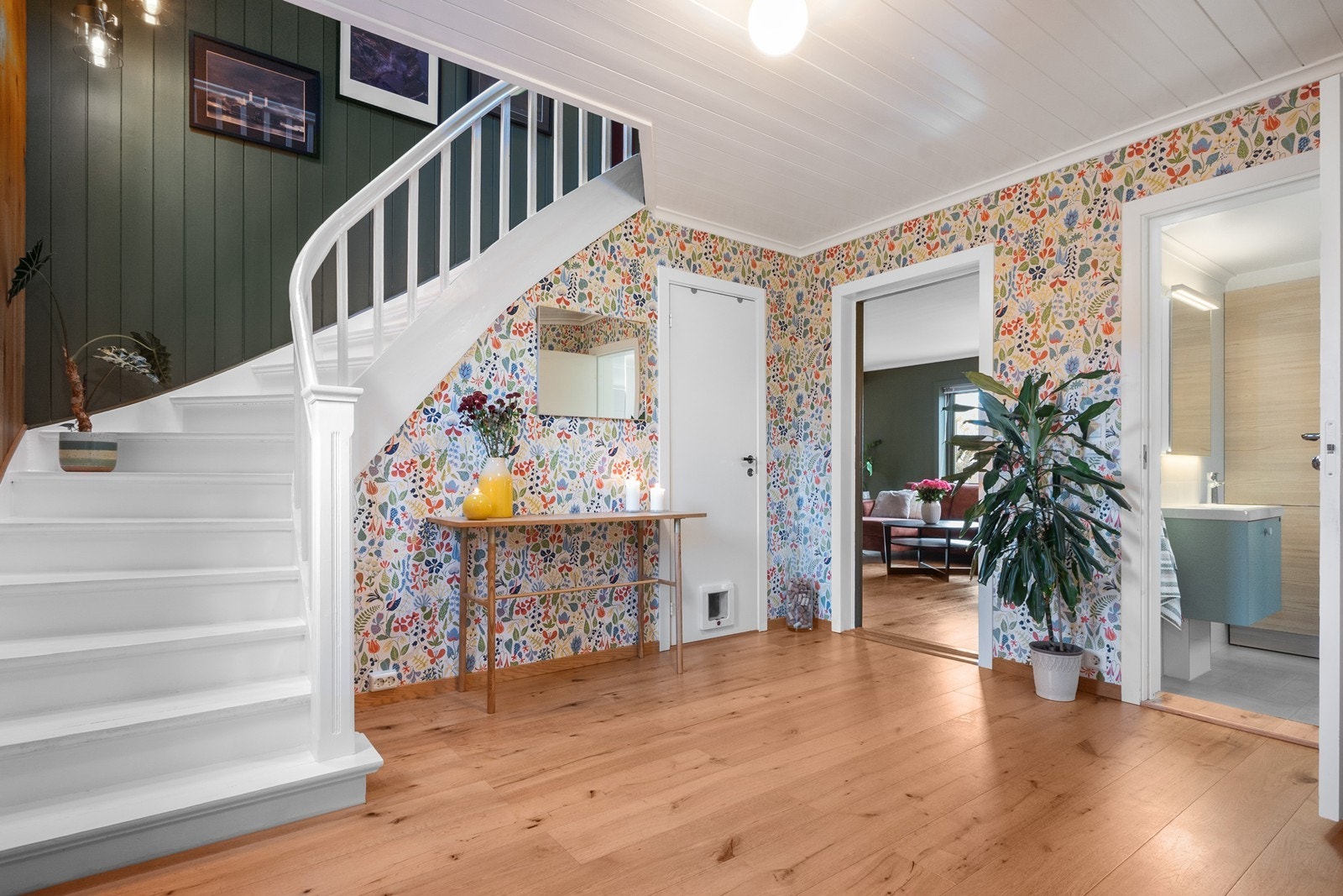 Videre åpner gangen seg med et sjarmerende tapet i fargerikt mønster og en elegant trapp som leder opp til boligens øvrige etasje. Galleribilde