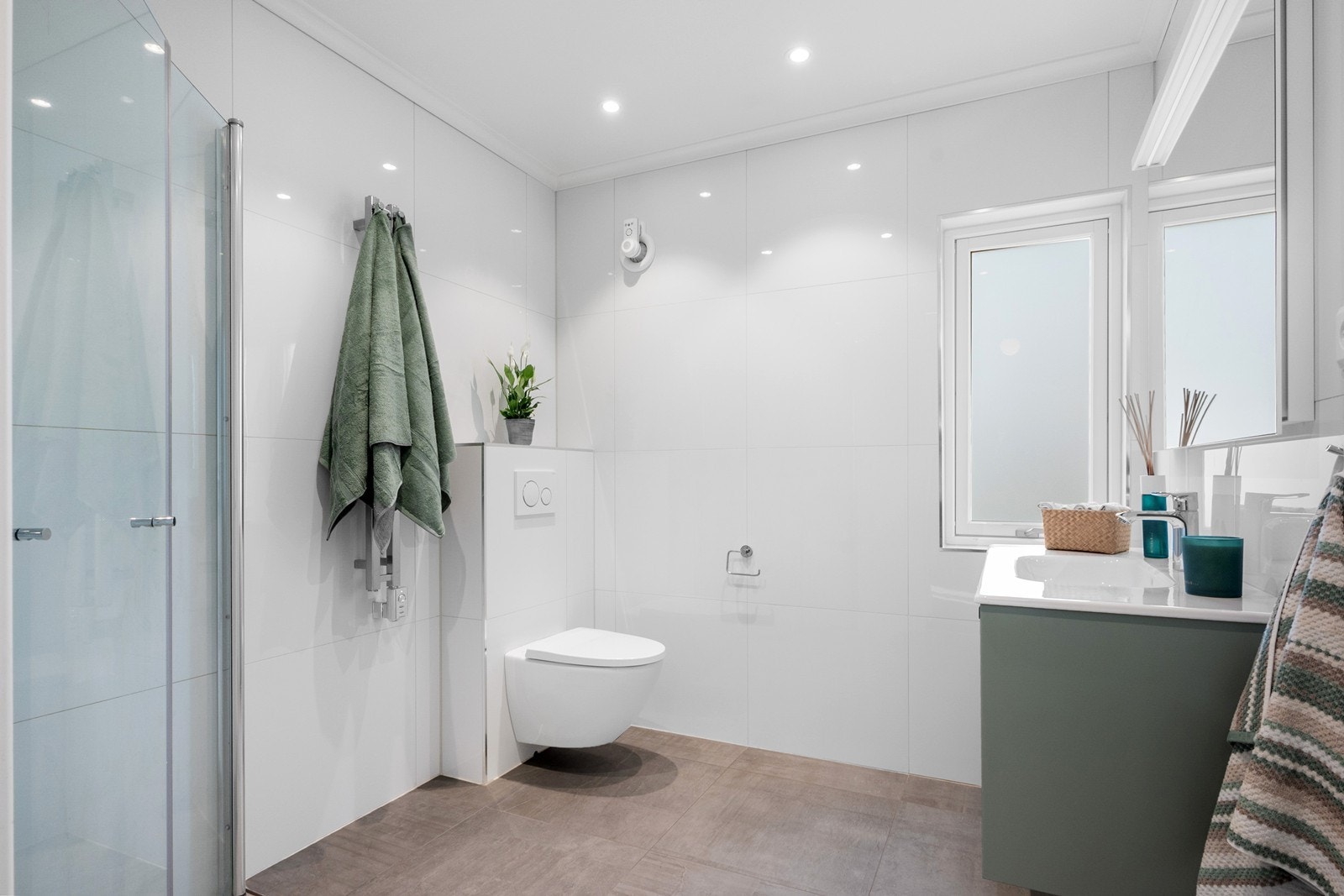 Badet fremstår moderne med store fliser i lyse toner, kombinert med servant i en dus grønntone. Galleribilde