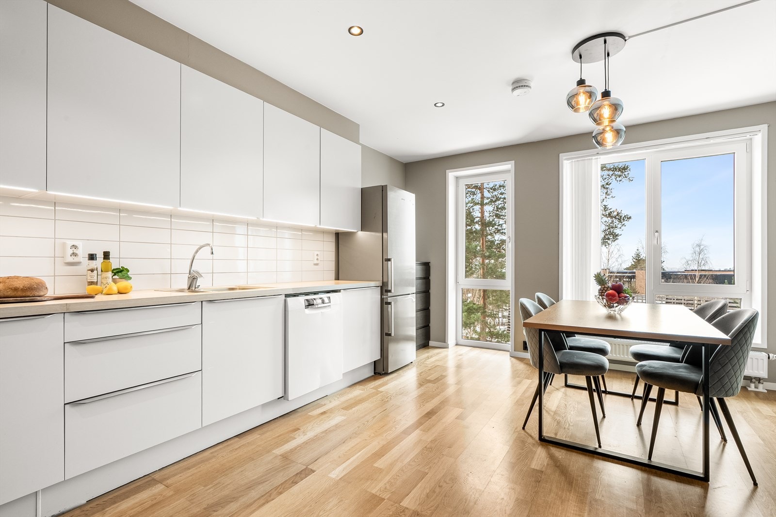 Stilrent kjøkken fra HTH. Det er montert kjøkkeninnredning med glatte folierte fronter, benkeplate i laminat med nedfelt kum i rustfritt stål, ledlys under overskap og flis på vegg over benkeplatene. Galleribilde